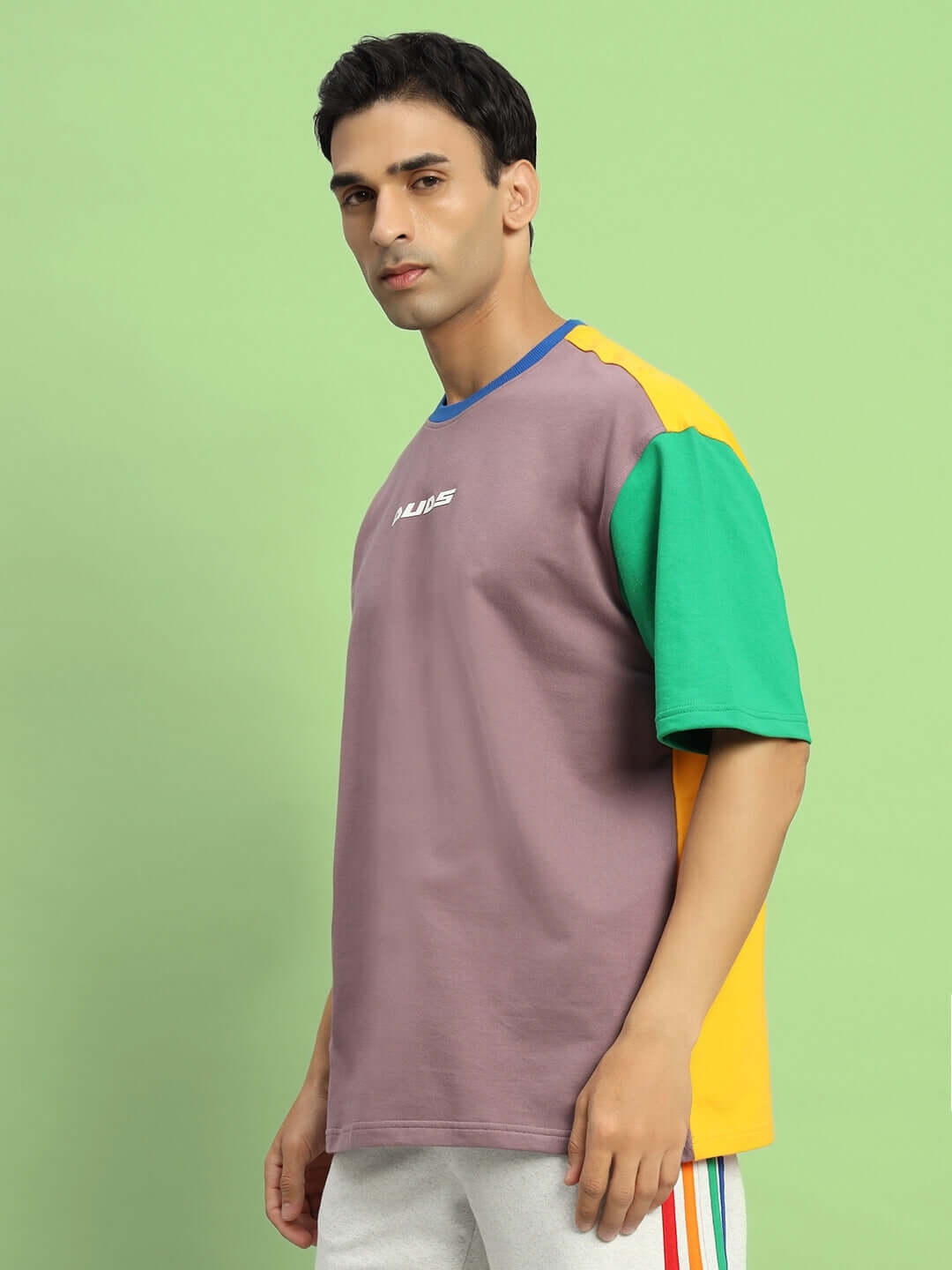 Man wearing IRIS color-blocked oversized t-shirt featuring premium cotton and elastane blend, styled in multi-color blocks, against a green background.