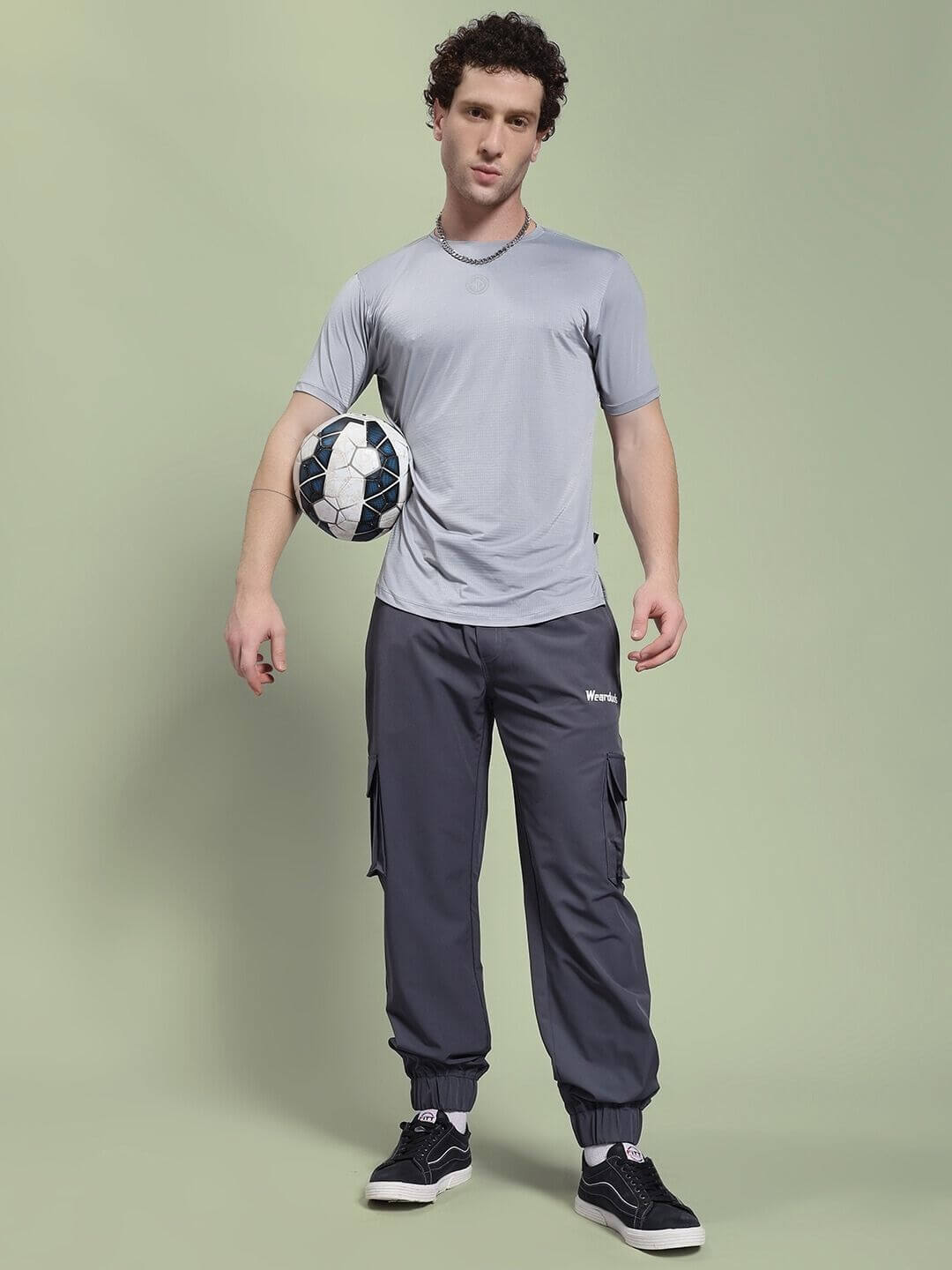 Model wearing JACK RELAXED FIT MULTI POCKET CARGO DARK GREY pants, showcasing sporty and casual style with a soccer ball.