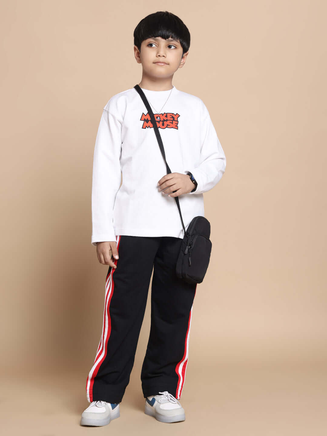 Child wearing JIMMIE oversized co-ord set in white-black with red panel joggers, styled with a crossbody bag, photographed on beige backdrop.