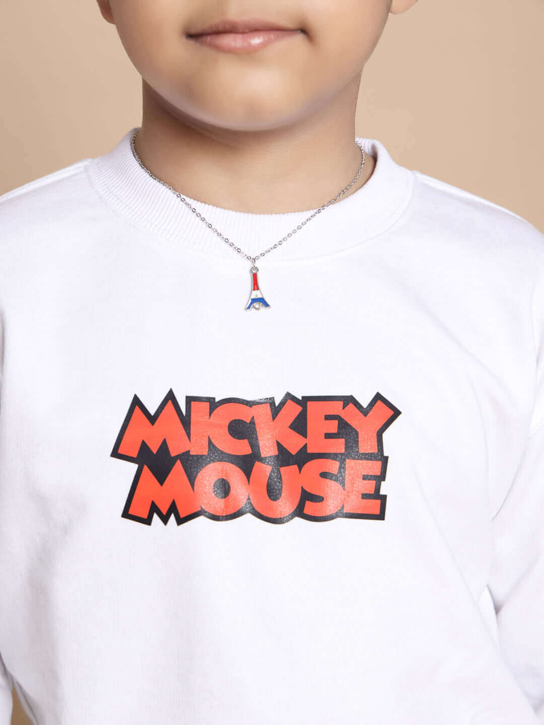 Child wearing a white sweatshirt with 'Mickey Mouse' print and a small Eiffel Tower necklace.