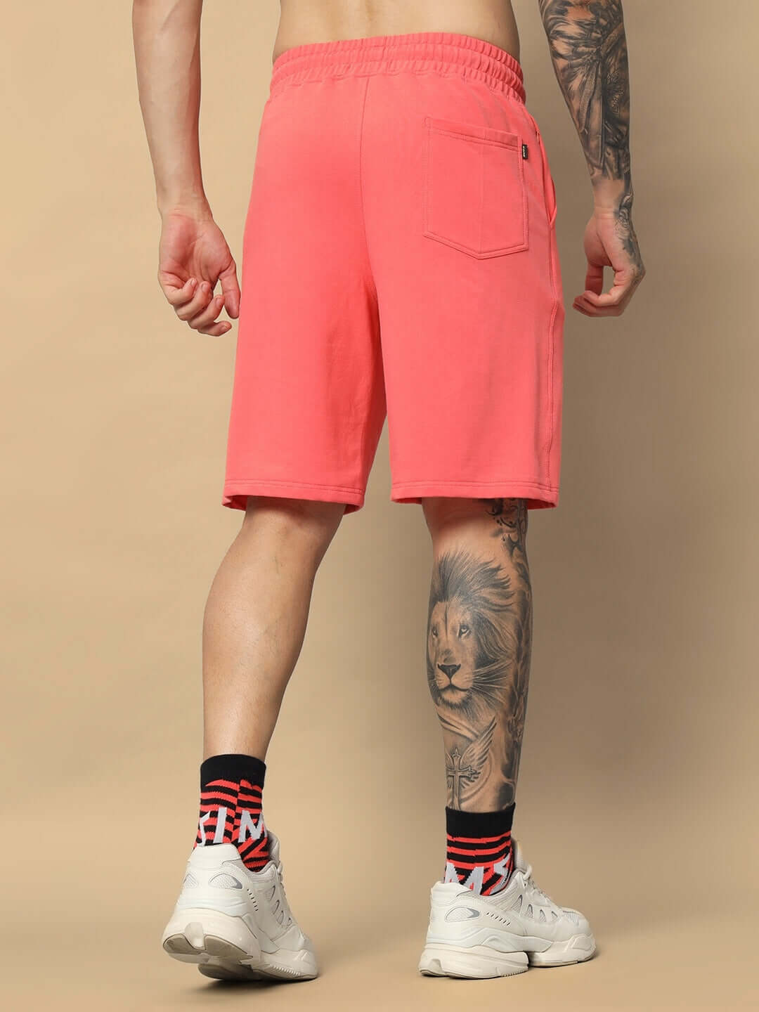 Back view of Joker Regular Fit Shorts in Pantone Peach, featuring elastic waistband and pocket, styled with white sneakers and tattoo sleeve.