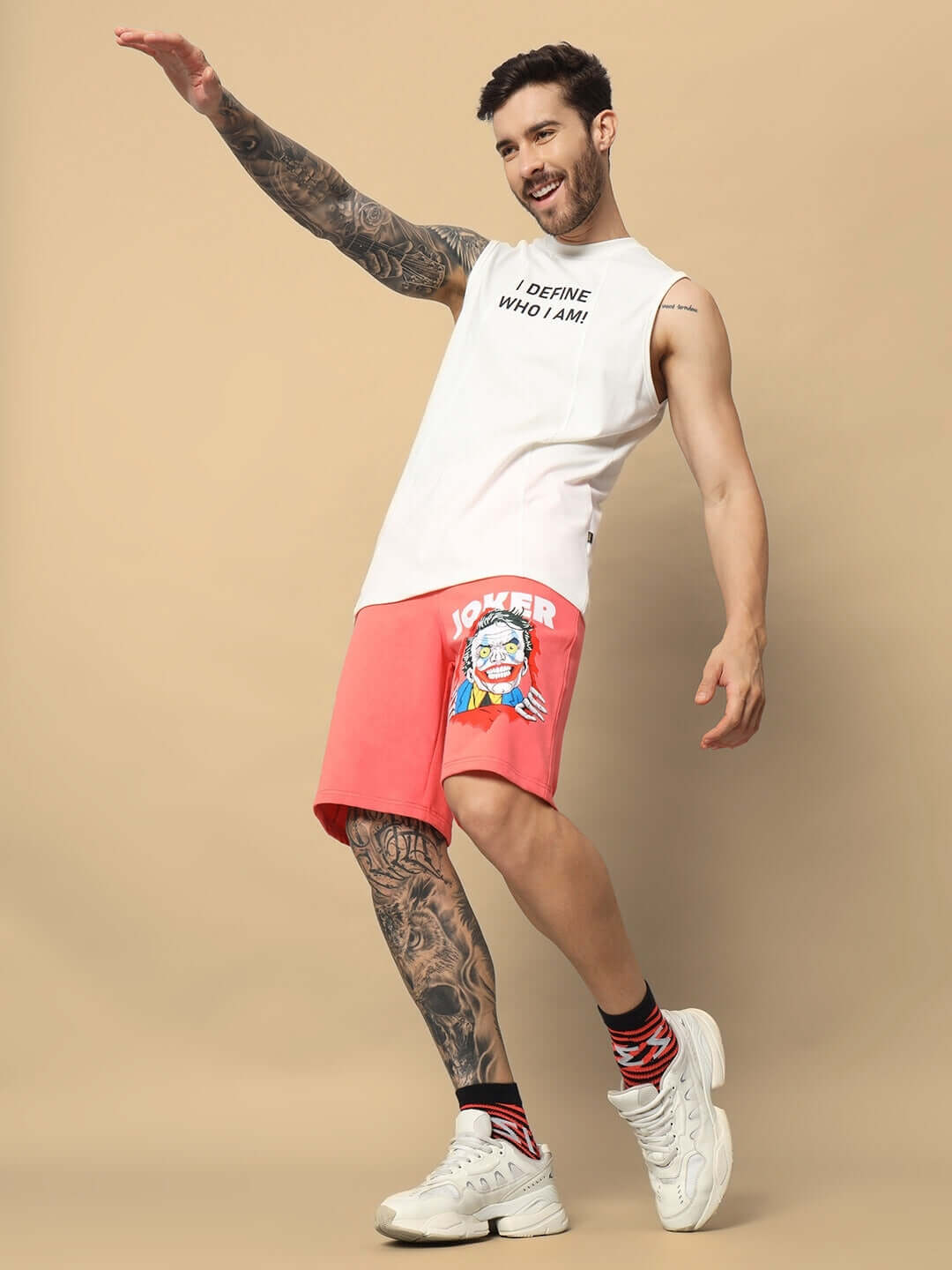 Man wearing Joker regular fit shorts in Pantone Peach, white tank top, posing playfully against beige background.