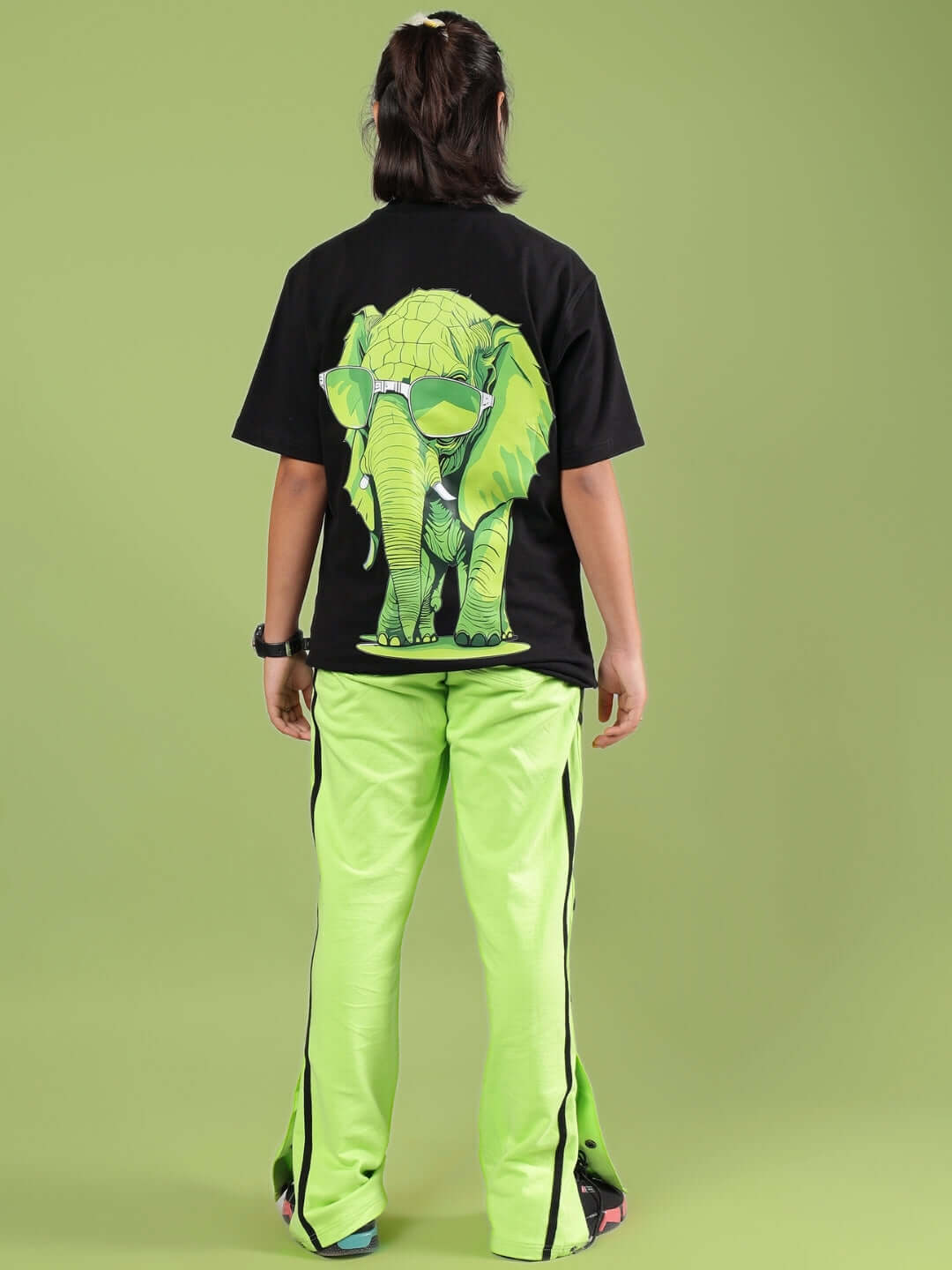 Child wearing JUMBO CO-ORD FOR BOYS & GIRLS BLACK-NEON outfit with elephant graphic on black shirt, green pants, rear view.