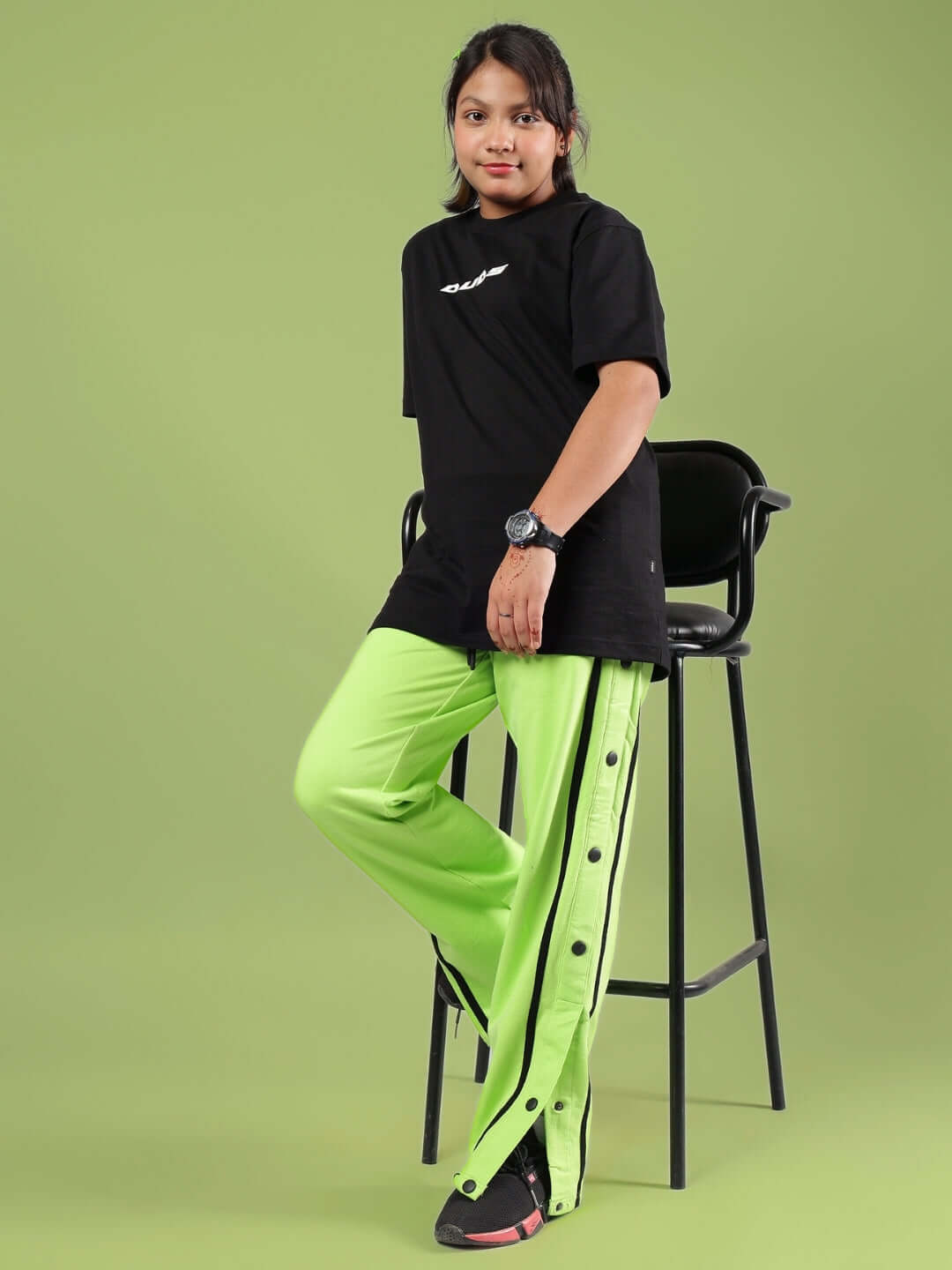 Child wearing JUMBO CO-ORD FOR BOYS & GIRLS BLACK-NEON standing by a chair, showcasing vibrant black and neon fashion ensemble.