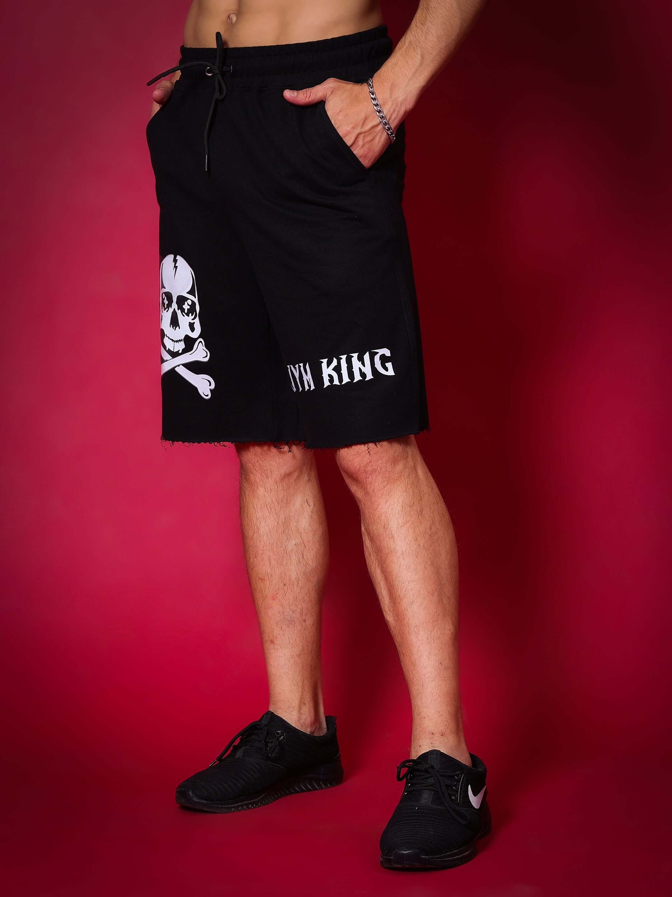 JYM KING black regular fit shorts with skull design, featuring customizable size options for a perfect fit, modeled against a red background.
