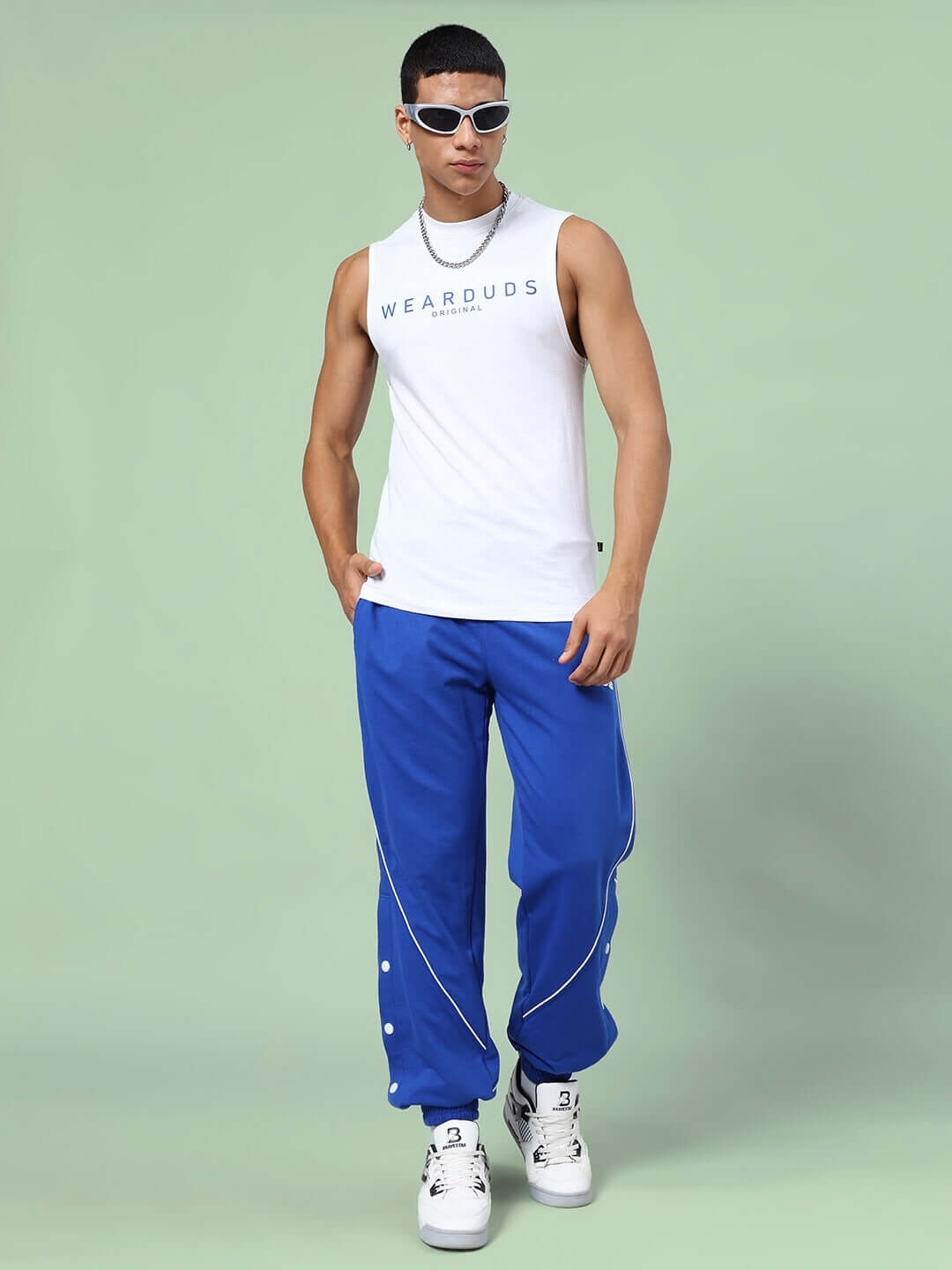 Model wearing KICKSHAW RELAXED FIT CO-ORD SET WHITE-R BLUE, featuring unisex relaxed fit joggers and white tank top with graphic text.