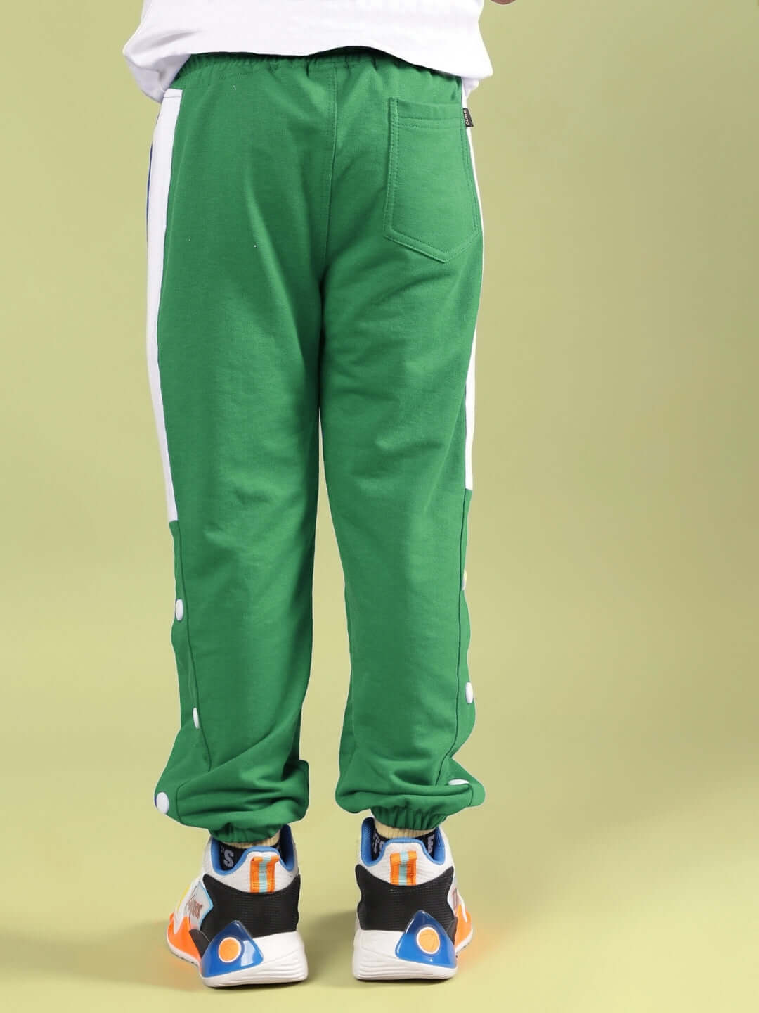 Child wearing green athletic pants with white stripes and colored sneakers, standing in front of a light green background.