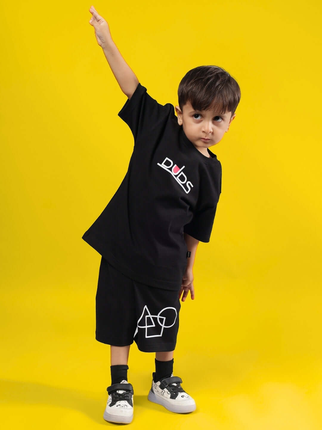 Child wearing a black SQUID BATTLE co-ord set by DUDS on a yellow background, featuring a playful pose.