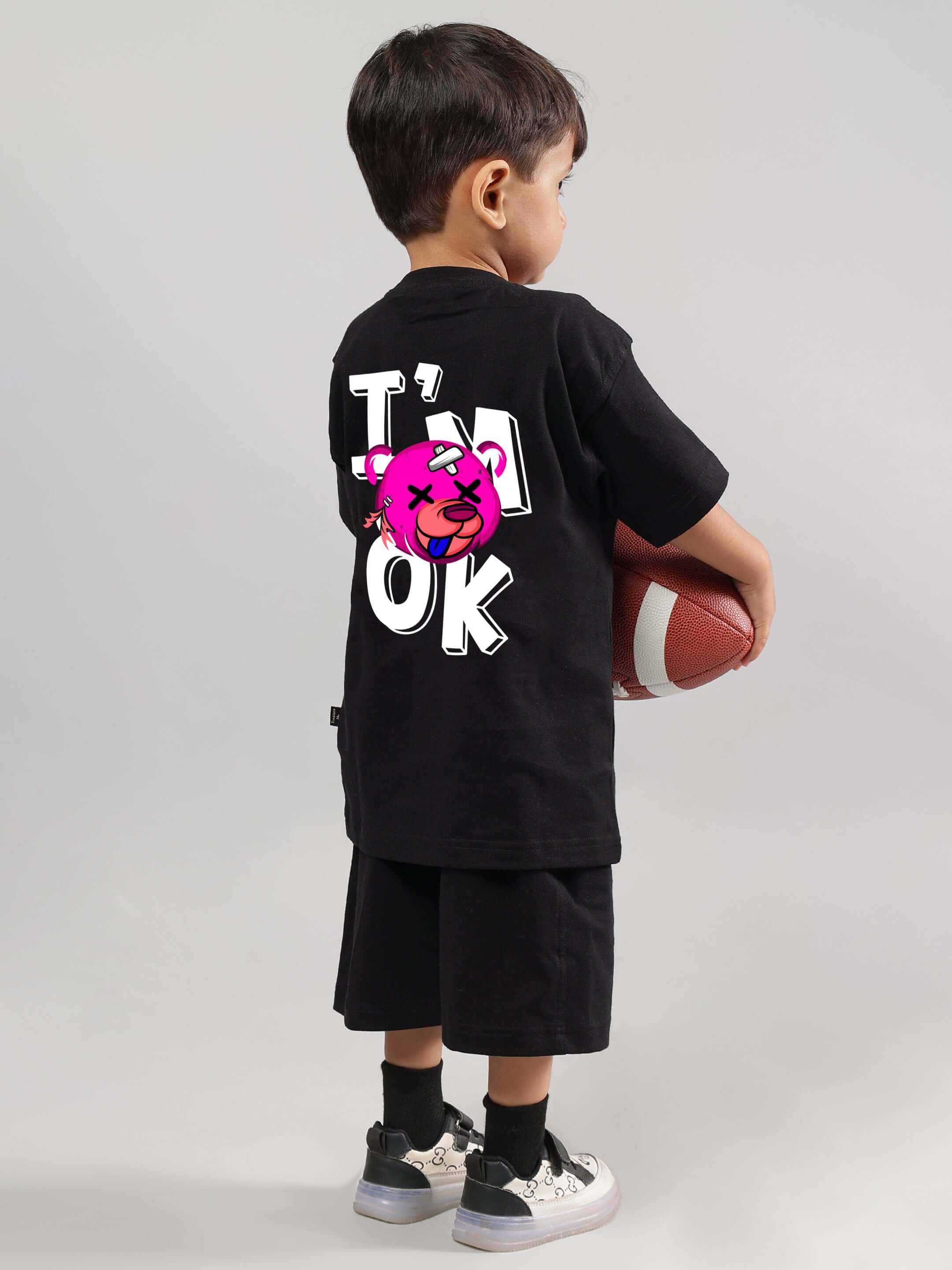Child wearing black I'M OK co-ord outfit holding football, showcasing comfortable fashion for boys and girls, made-to-order by DUDS.