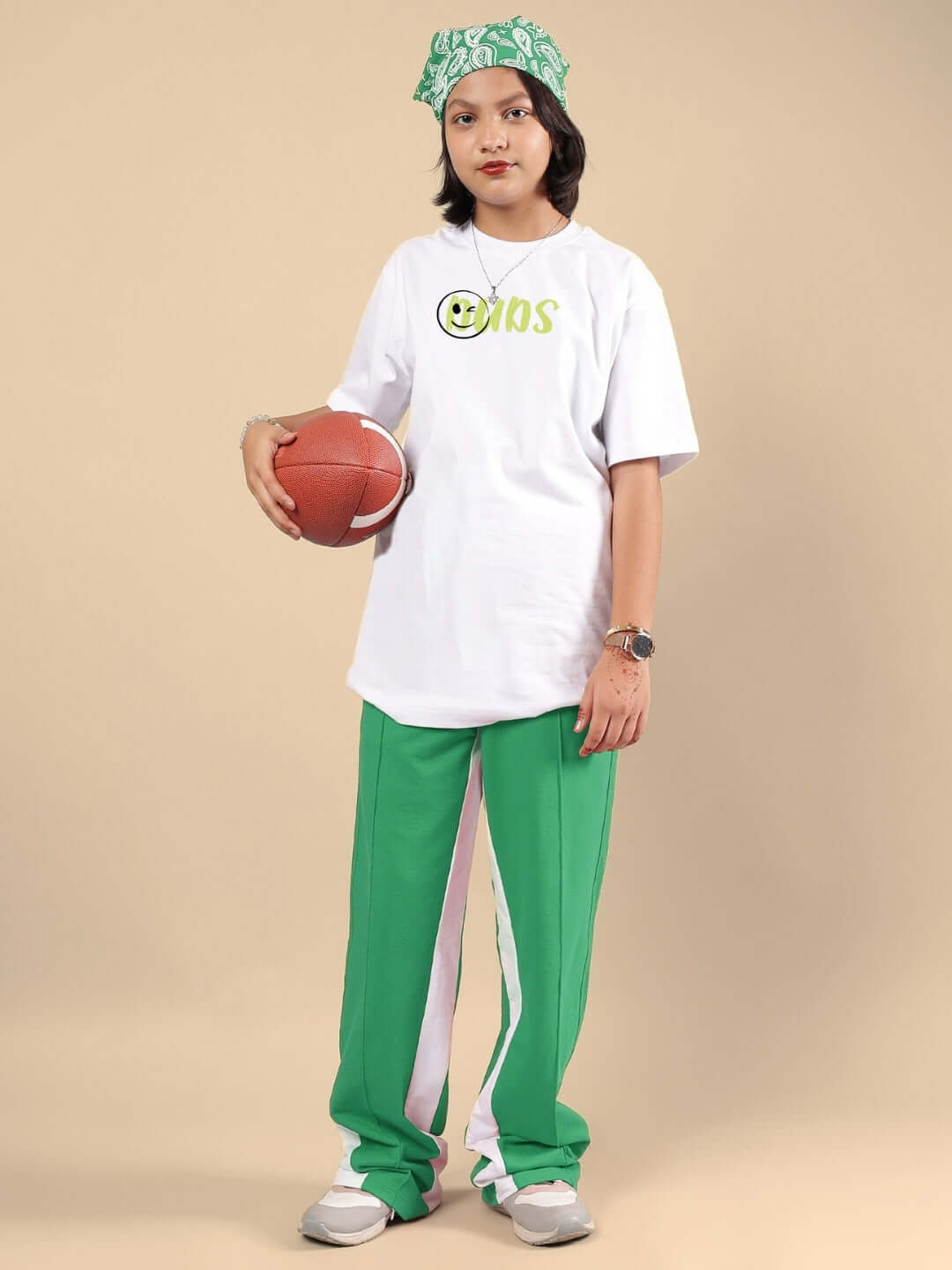 Youth wearing white-green co-ord outfit, holding a basketball, standing on beige background. Unisex fashion apparel by DUDS.