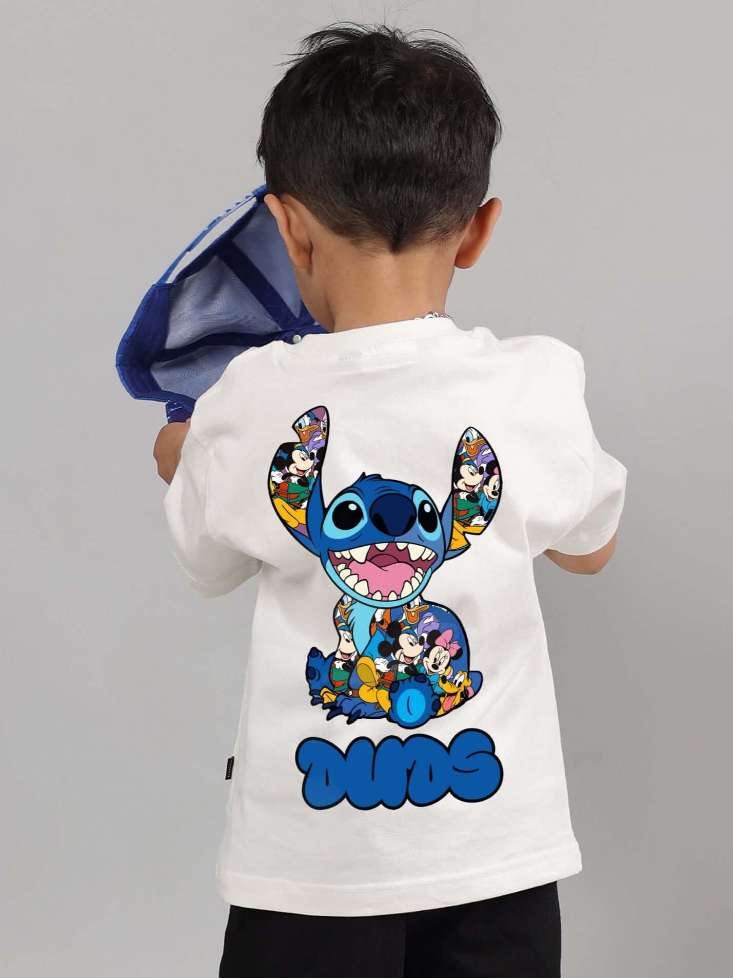 Child wearing an off-white DUDS t-shirt with vibrant print cartoon characters on the back, designed for boys and girls. Made to order.