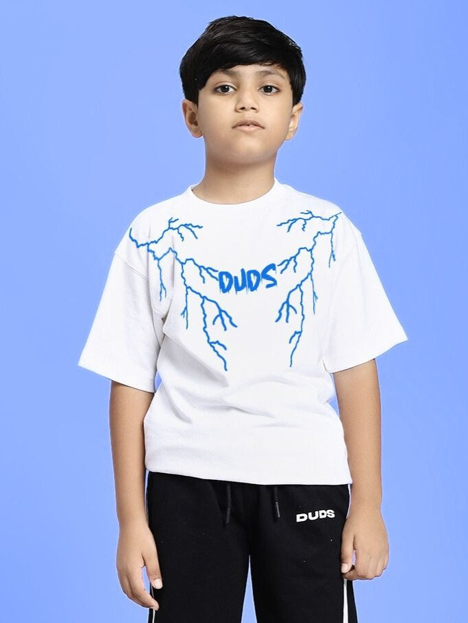 Boy wearing a white t-shirt with blue design and black pants against a blue background.