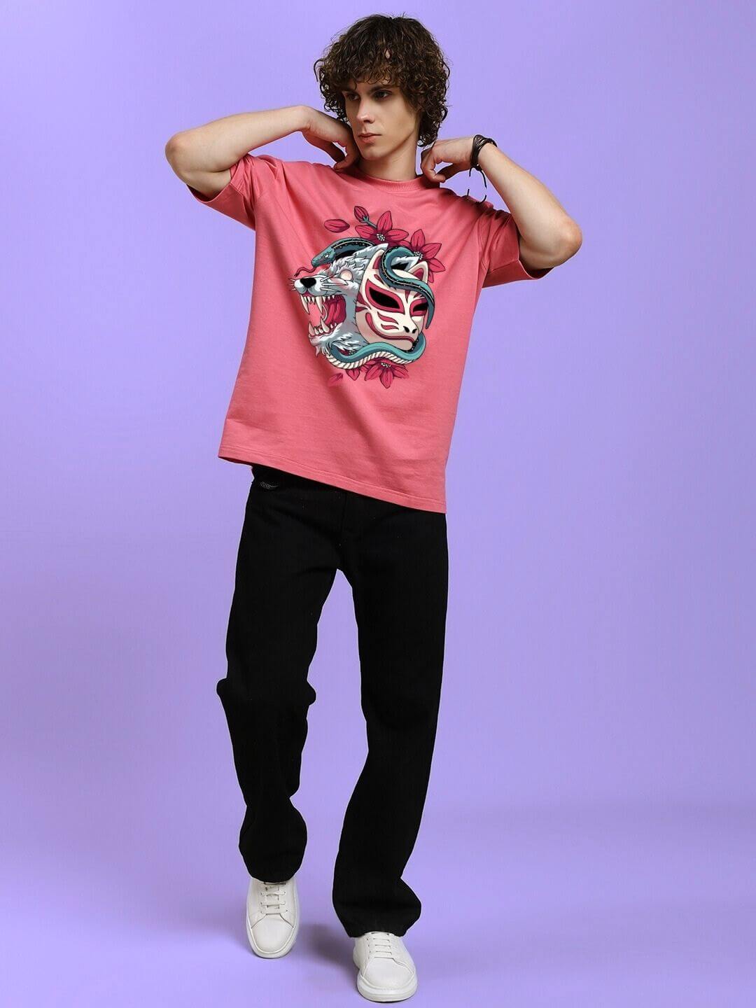 Man wearing KITSUNE WOLF PRINTED OVERSIZED T-SHIRT PINK with wolf motif, standing in stylish pose against purple background.