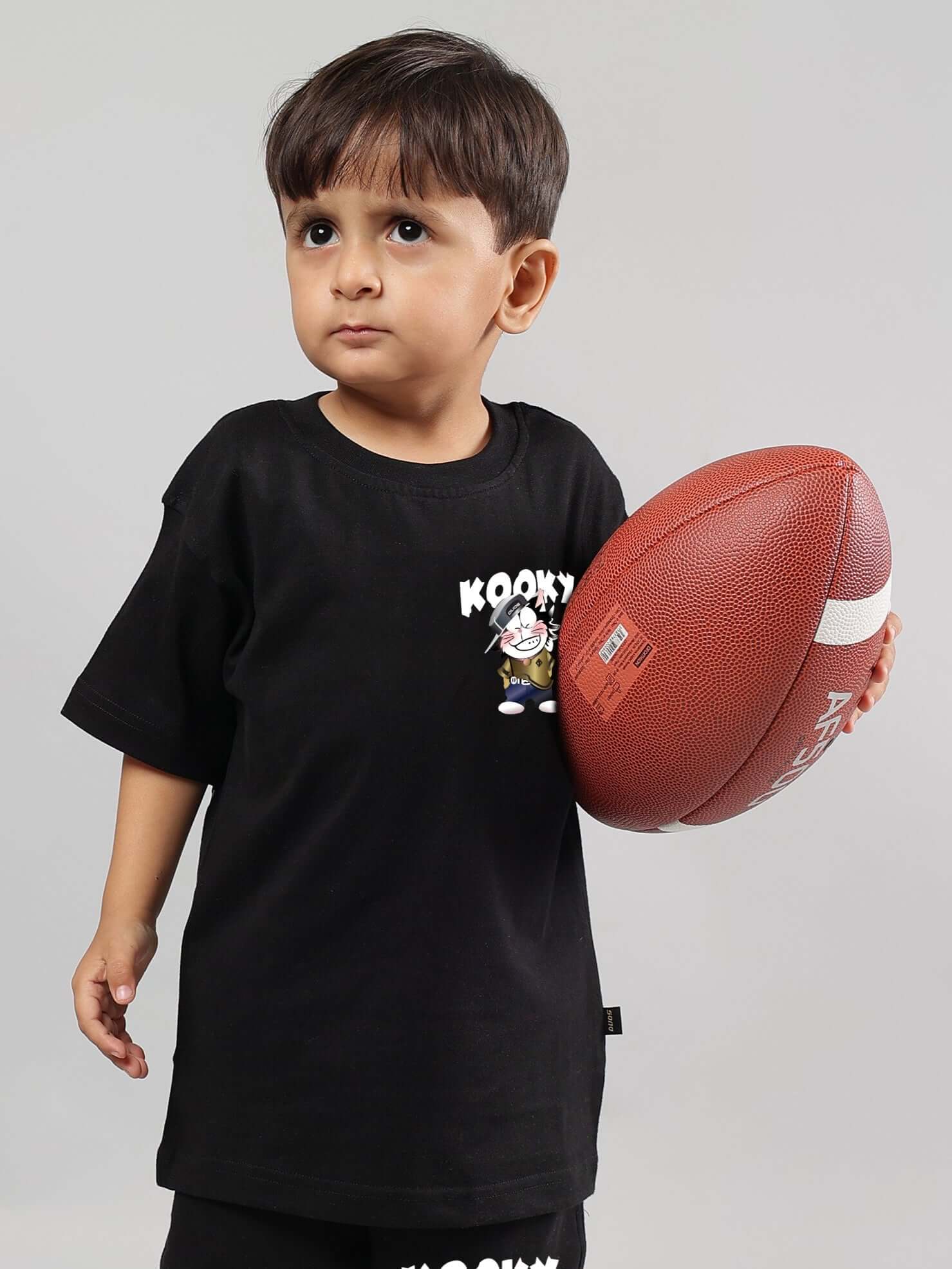 Young child wearing a KOOKY black t-shirt holding a football, showcasing custom fit options for boys and girls.