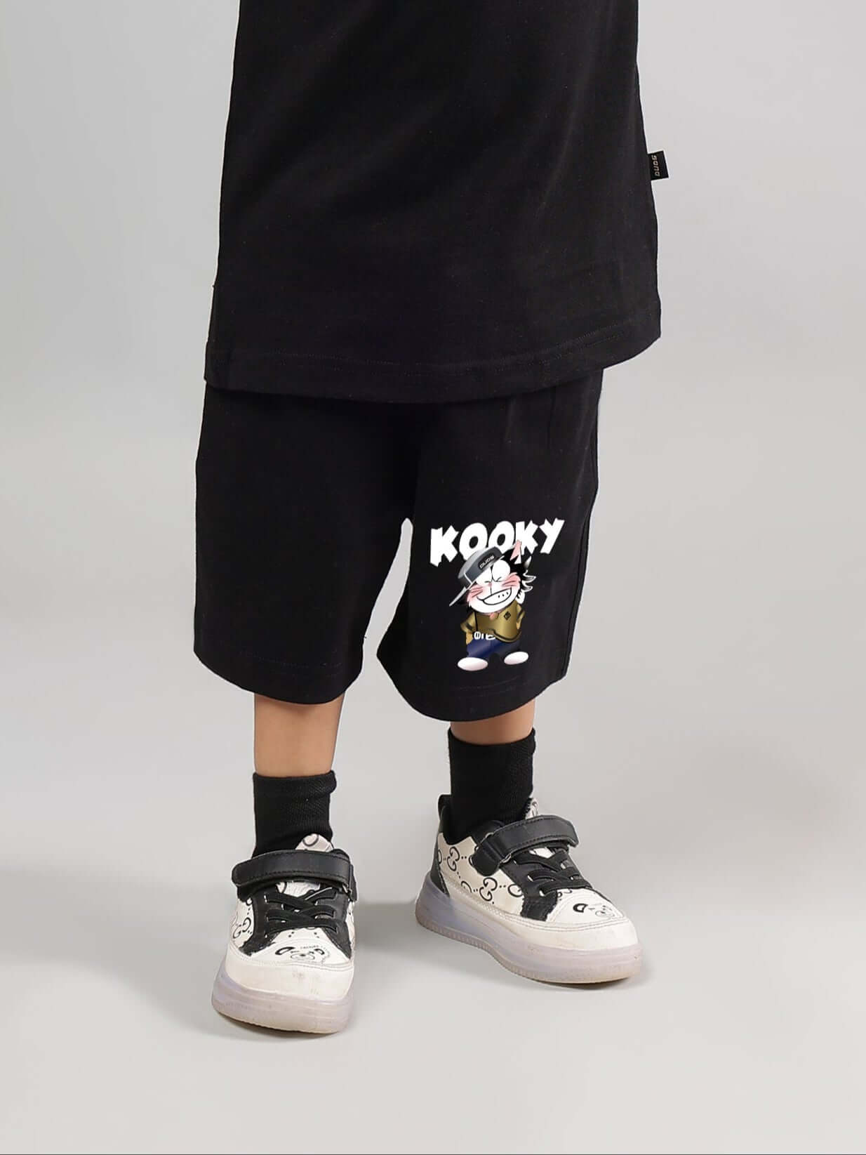 Child wearing Kooky black shorts with cartoon graphic, styled with black socks and sneakers.