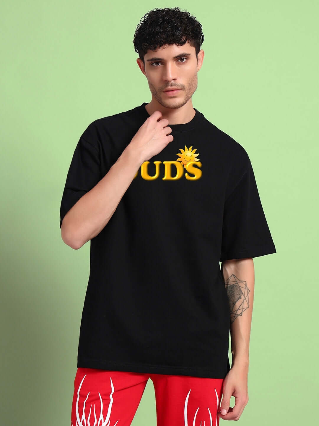 Person wearing LABUBU Monsters oversized black T-shirt made of heavy gauge fabric, paired with red pants against a green background.
