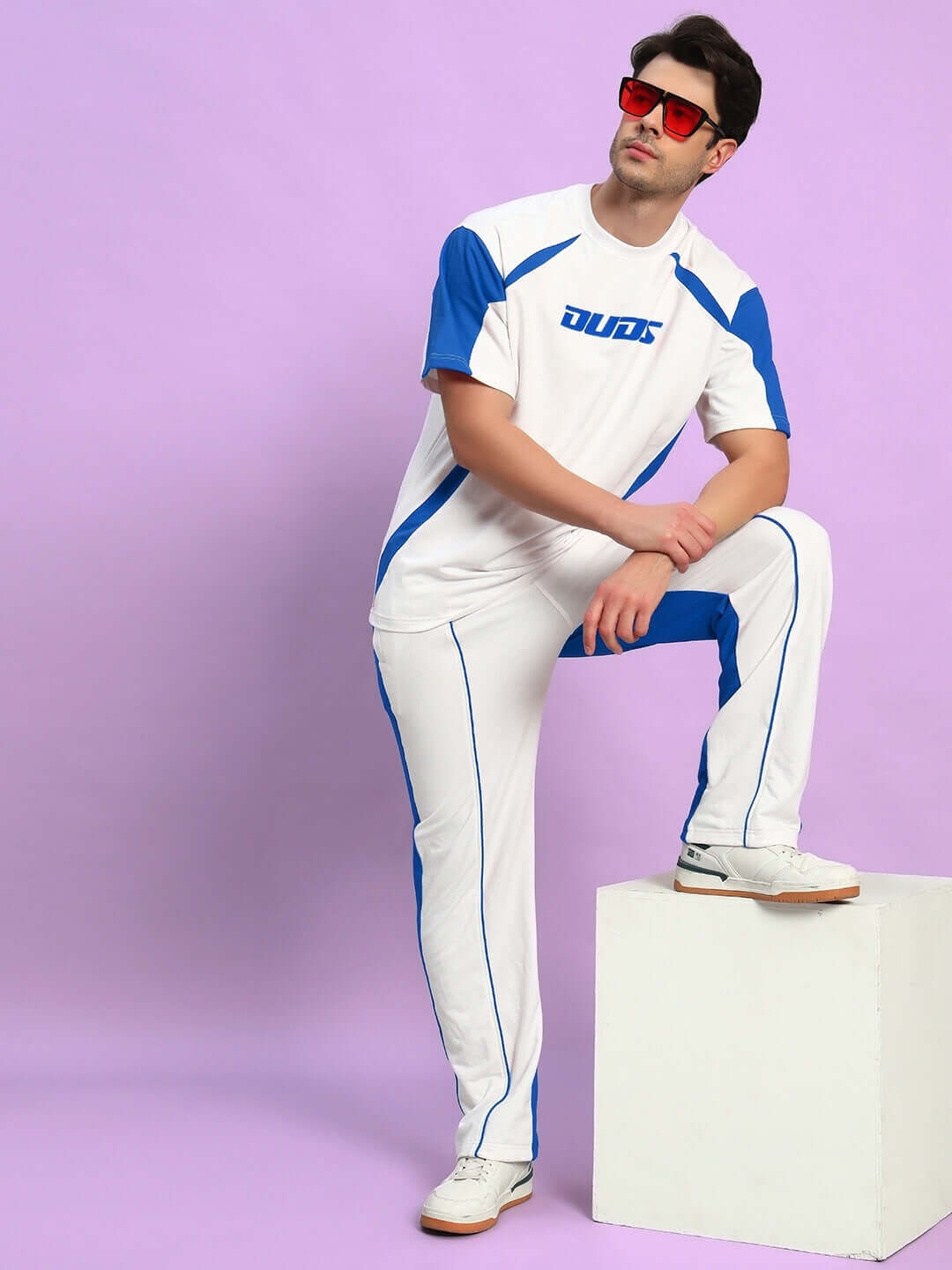 Model wearing LAGOON RELAXED FIT JOGGERS WHITE BLUE with blue accents, standing against a purple backdrop.