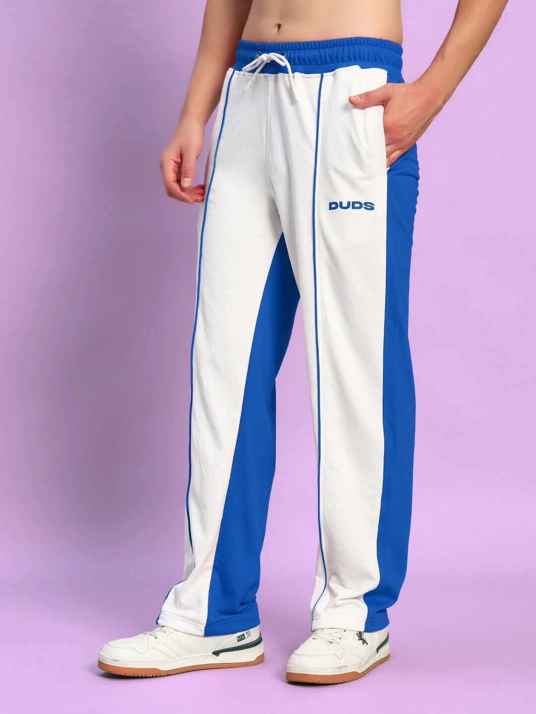Model wearing LAGOON RELAXED FIT JOGGERS WHITE BLUE showcased with casual sneakers against a purple background.