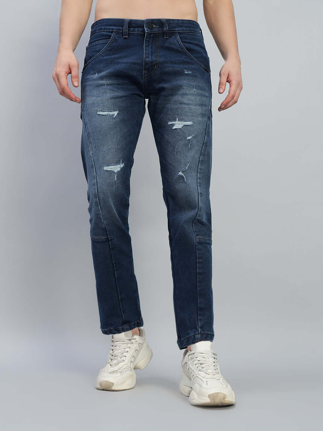 Model wearing Lavish Regular Fit Denim Jeans in blue with distressed detailing, paired with white sneakers, showcasing casual style.