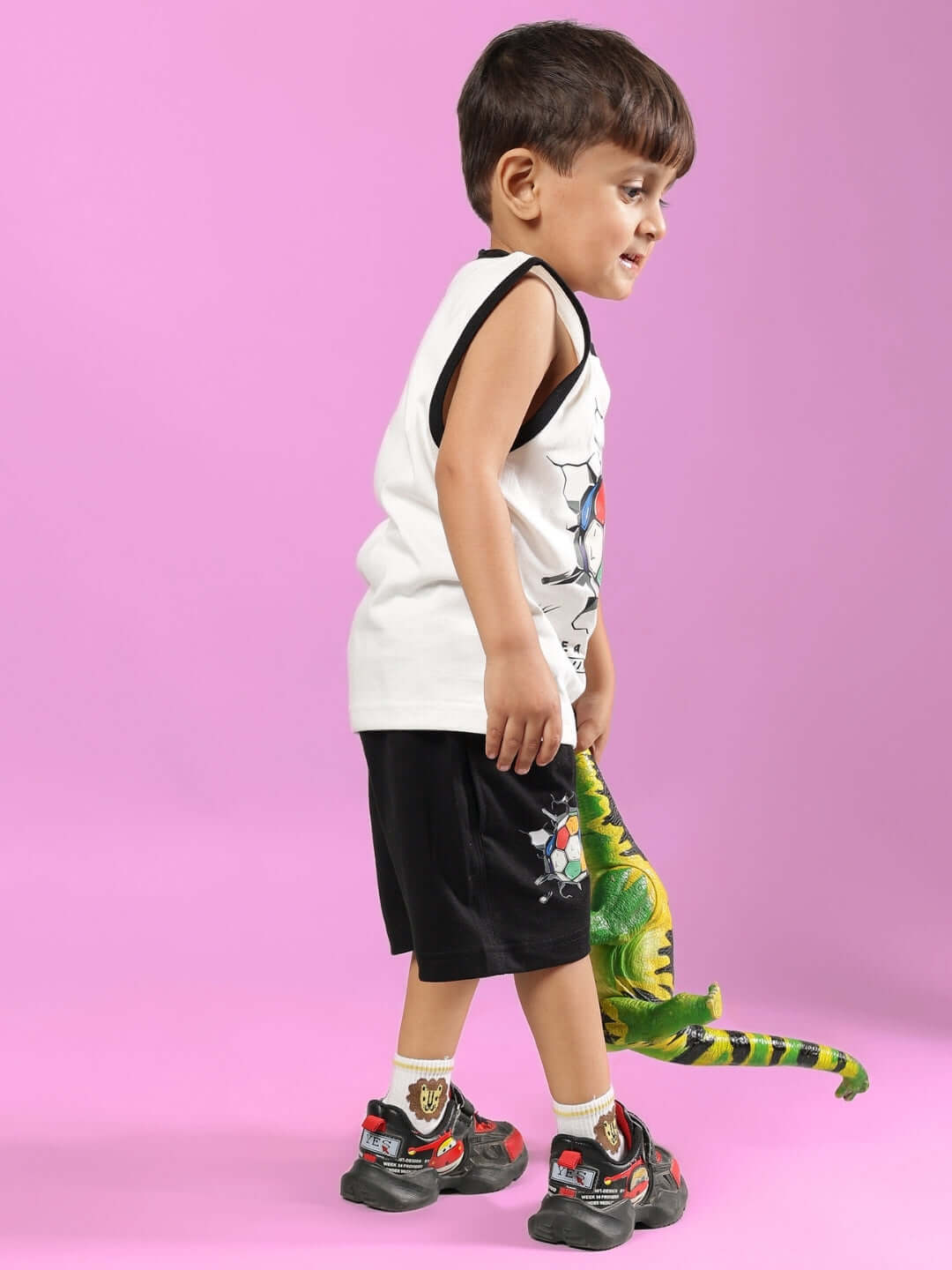 Young boy in LAZIO CO-ORD FOR BOYS & GIRLS OFF WHITE-BLACK set, holds toy dinosaur against pink background.
