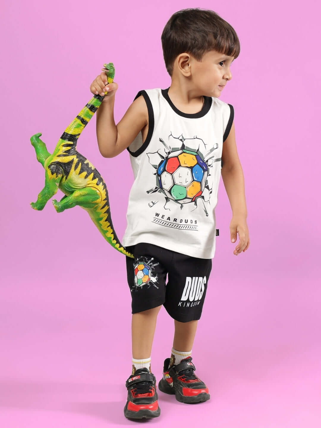 Young boy in LAZIO CO-ORD FOR BOYS & GIRLS OFF WHITE-BLACK outfit holds a toy dinosaur against a pink background, showcasing playful style.