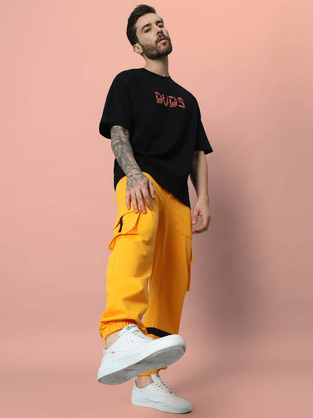 Model wearing a black Leo Puff Print oversized T-shirt and bright yellow cargo pants, showcasing urban streetwear fashion against a pink backdrop.