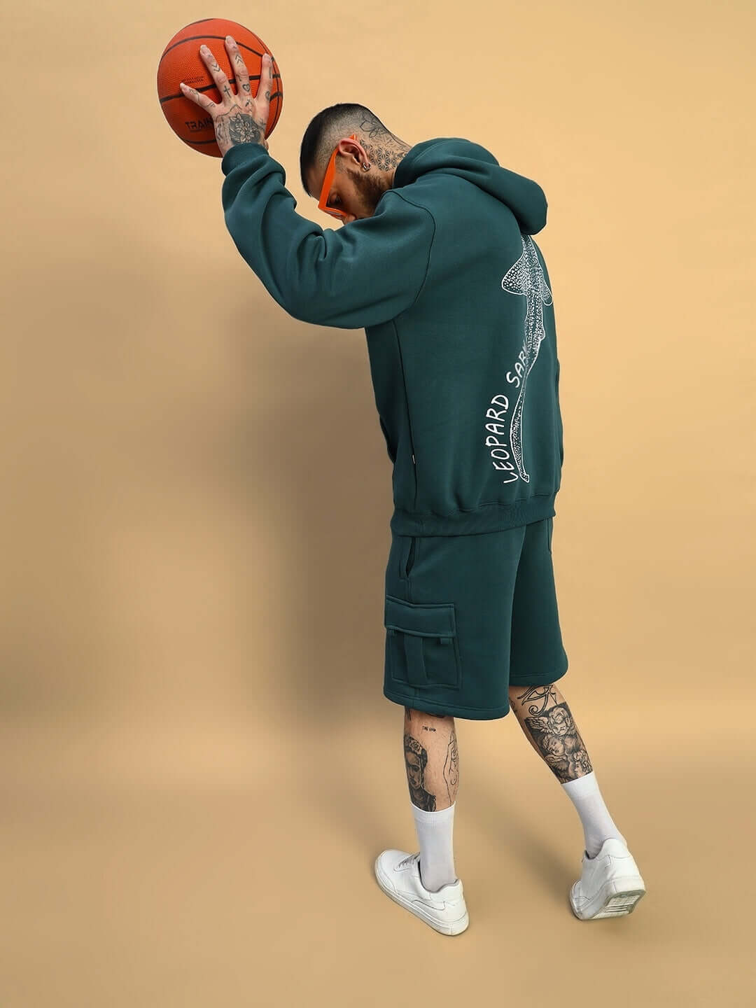 Man wearing LEOPARD SHARK FLEECE HOODIE TEAL GREEN and shorts, holding a basketball, back view.