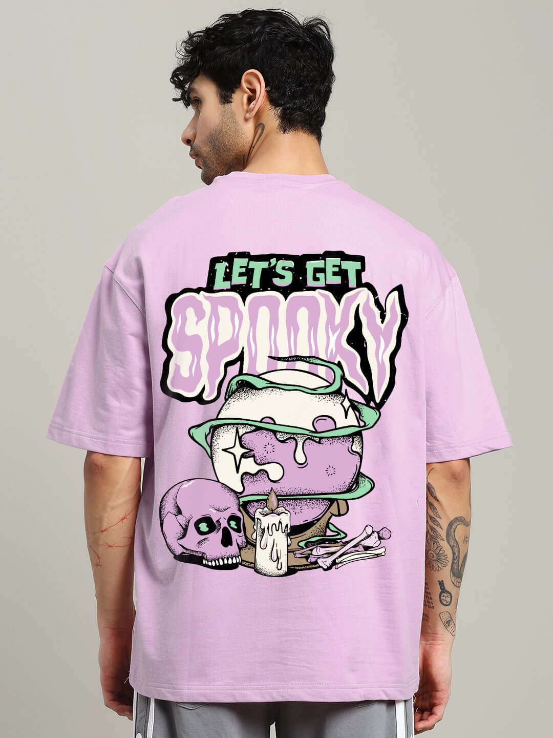 Back view of lavender oversized t-shirt with 'Let's Get Spooky' print, featuring a cauldron, skull, and candle graphics.