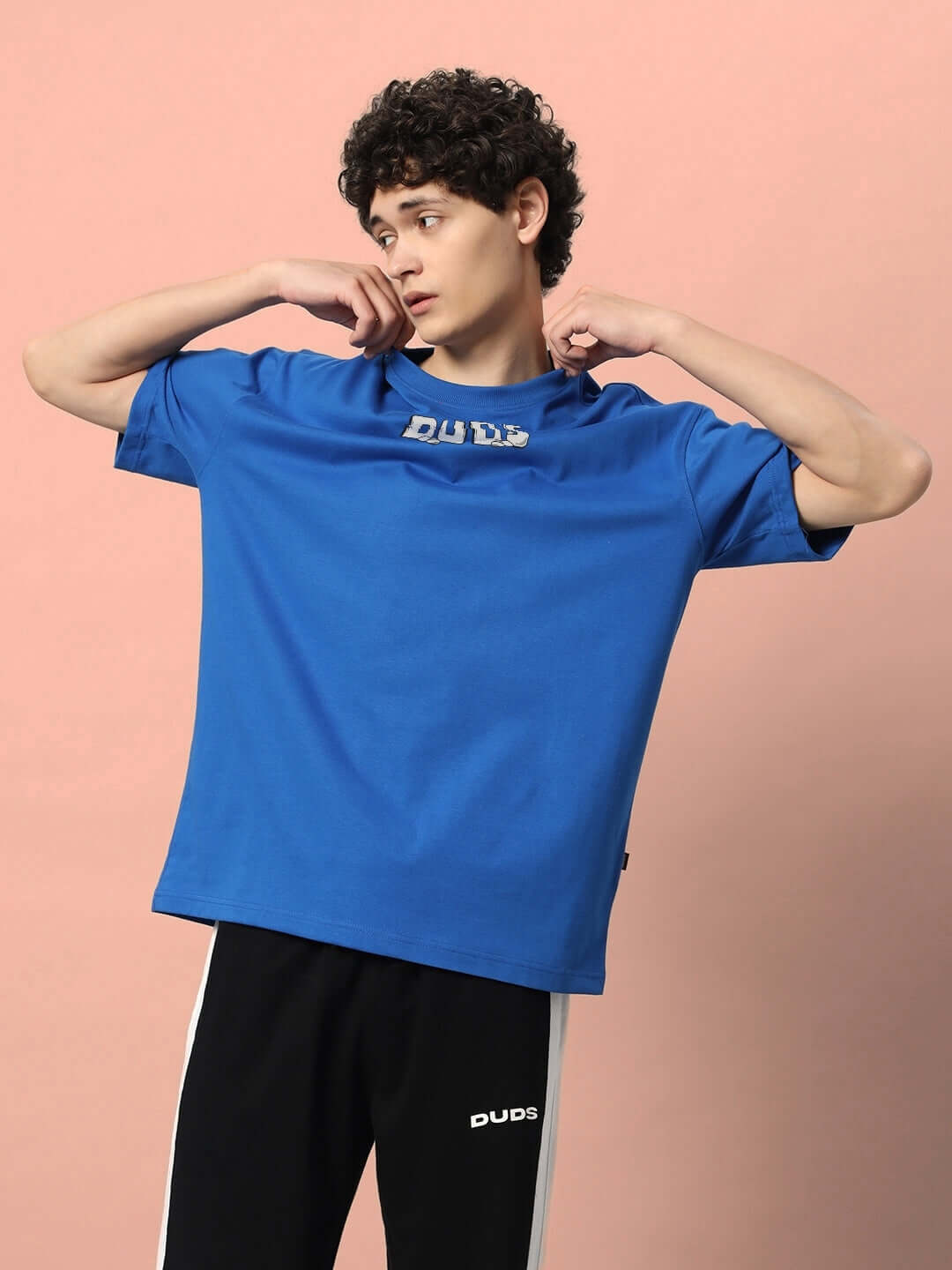 Model wearing LETS ROCK OVER-SIZED T-SHIRT ROYAL BLUE with relaxed fit, graphic design on pastel background.