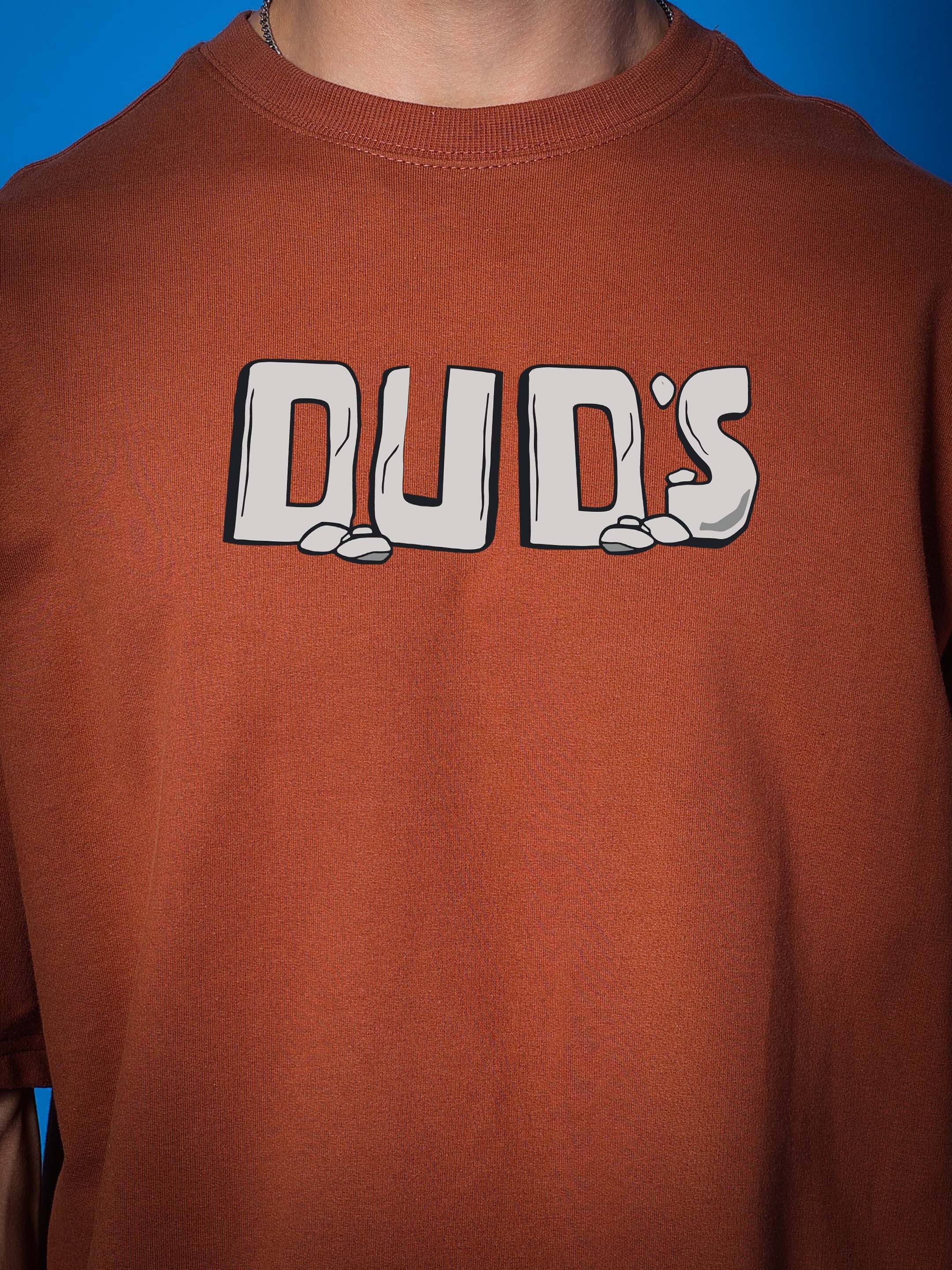 Brown oversized t-shirt with "DUD'S" graphic, made from premium cotton French terry fabric. Ideal for a relaxed and stylish look.