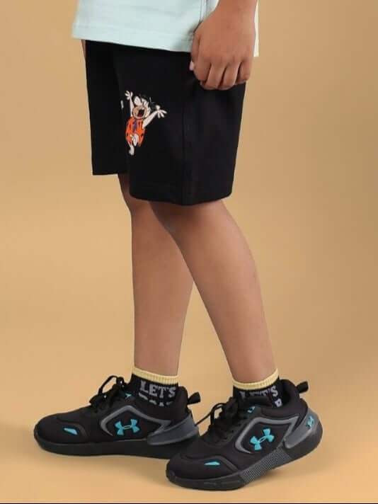 Child wearing LET'S ROCK SHORTS FOR BOYS & GIRLS BLACK, featuring playful illustration, standing against a beige background, stylish and comfortable.