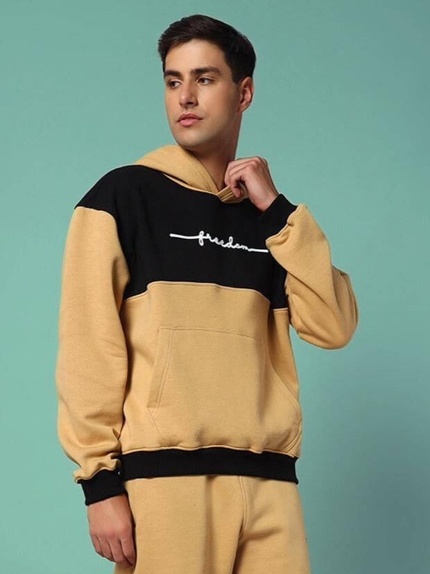 Man wearing LIBERTY FLEECE COLORBLOCK HOODIE BEIGE BLACK, showcasing modern streetwear style with bold colorblocking design.