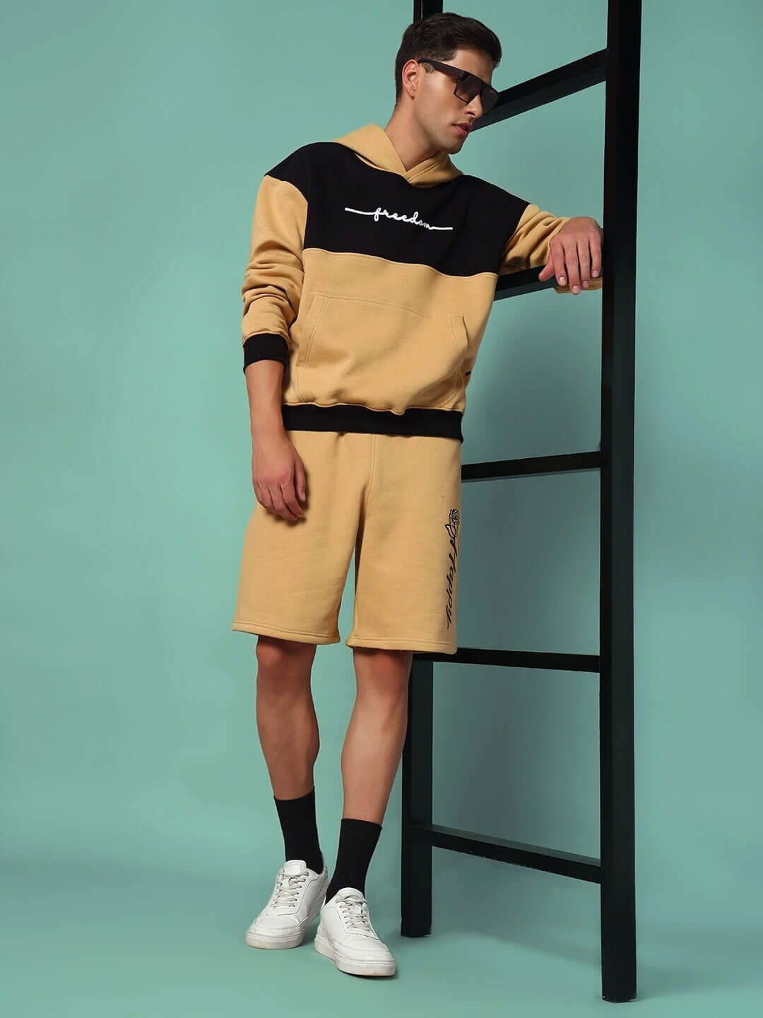 Model wearing LIBERTY FLEECE COLORBLOCK HOODIE BEIGE BLACK with matching shorts, showcasing modern streetwear style.