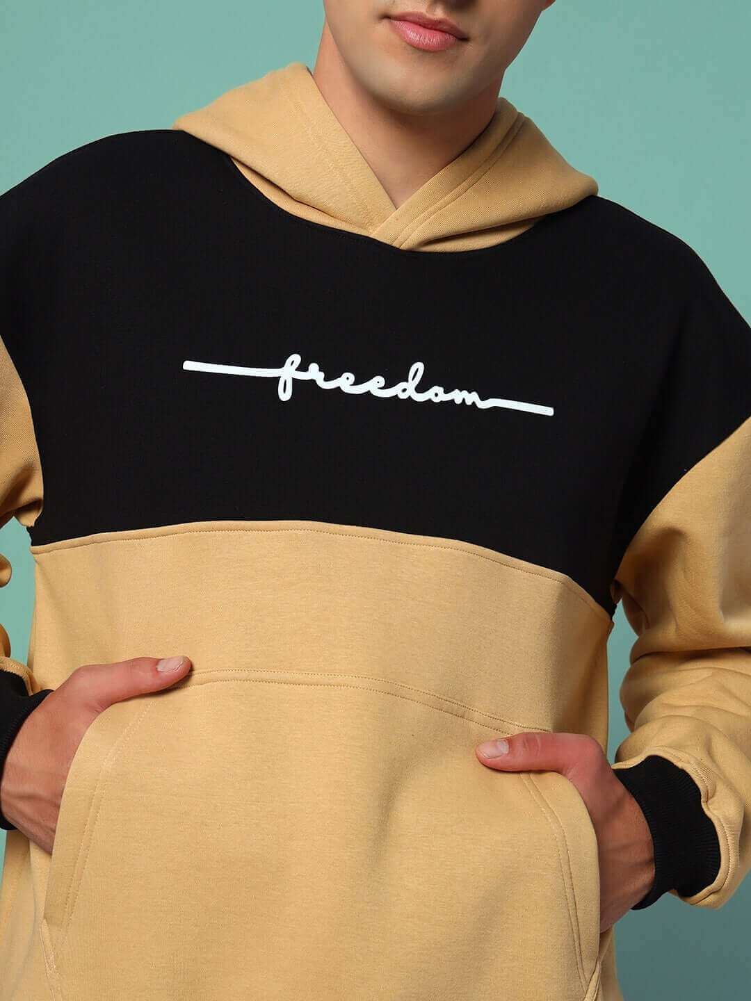 Man wearing LIBERTY FLEECE COLORBLOCK HOODIE BEIGE BLACK with freedom print, showcasing minimalistic streetwear style.