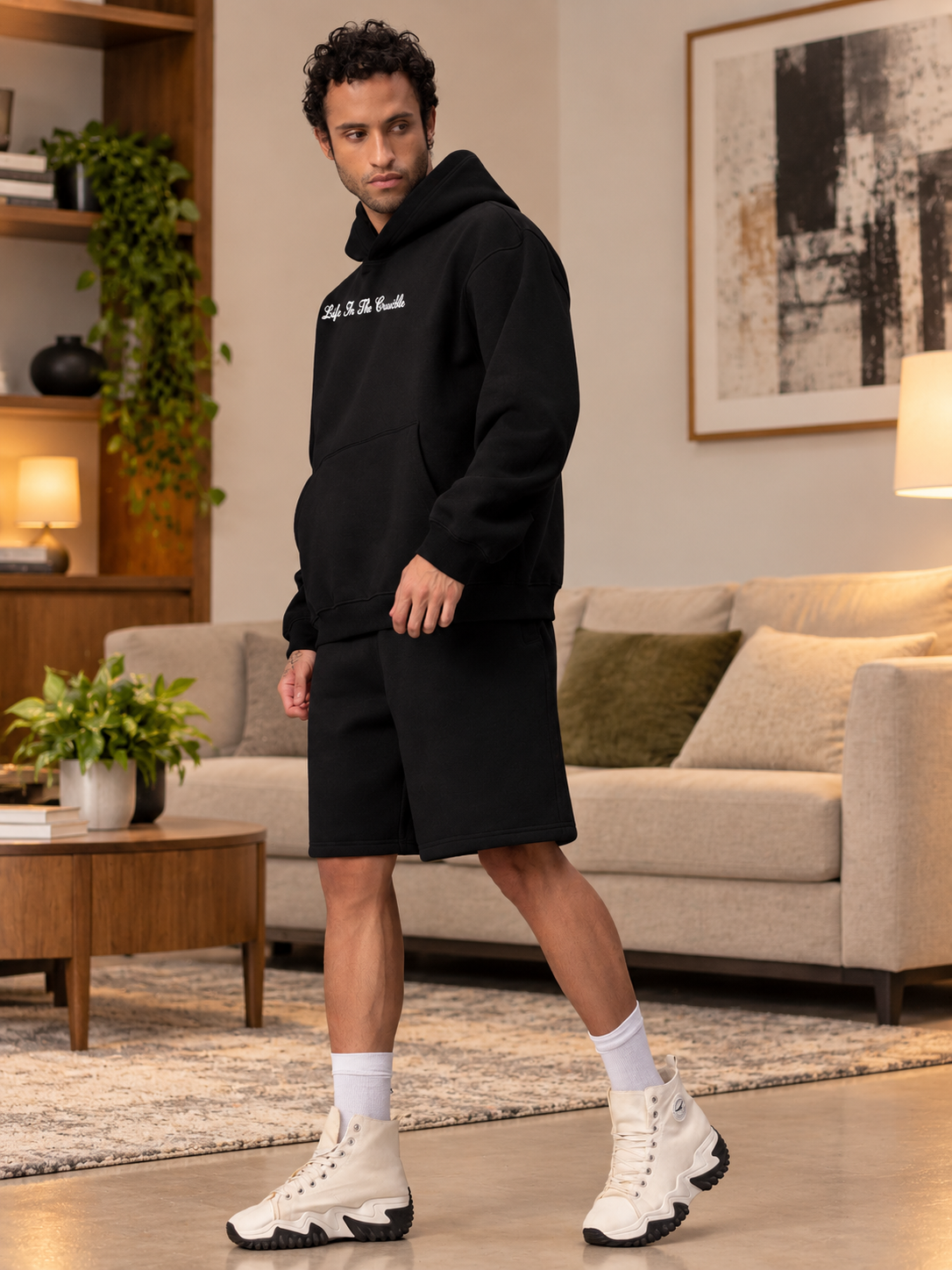 Man wearing LIFE IN THE CRUCIBLE PRINTED FLEECE CO-ORD BLACK hoodie and shorts set in a stylish living room