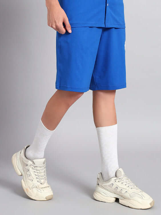 Model wearing blue LIMBO summer shorts with white sneakers and socks for casual style.