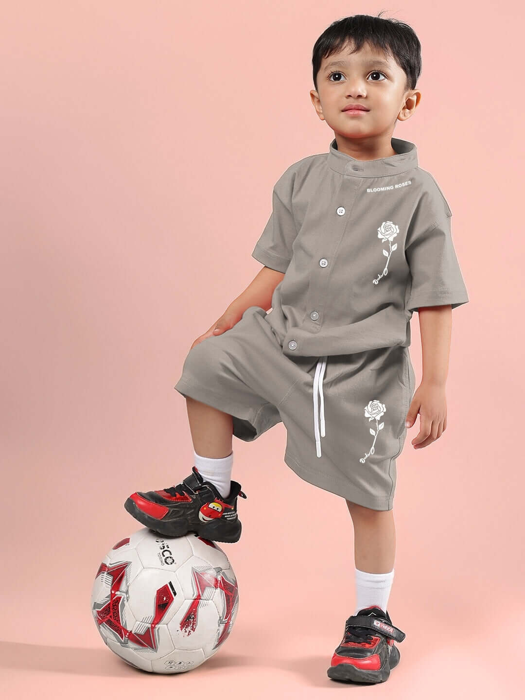 Child wearing grey LIMBO co-ord set with floral design, standing with foot on football, showcasing DUDS' custom fit clothing for kids.