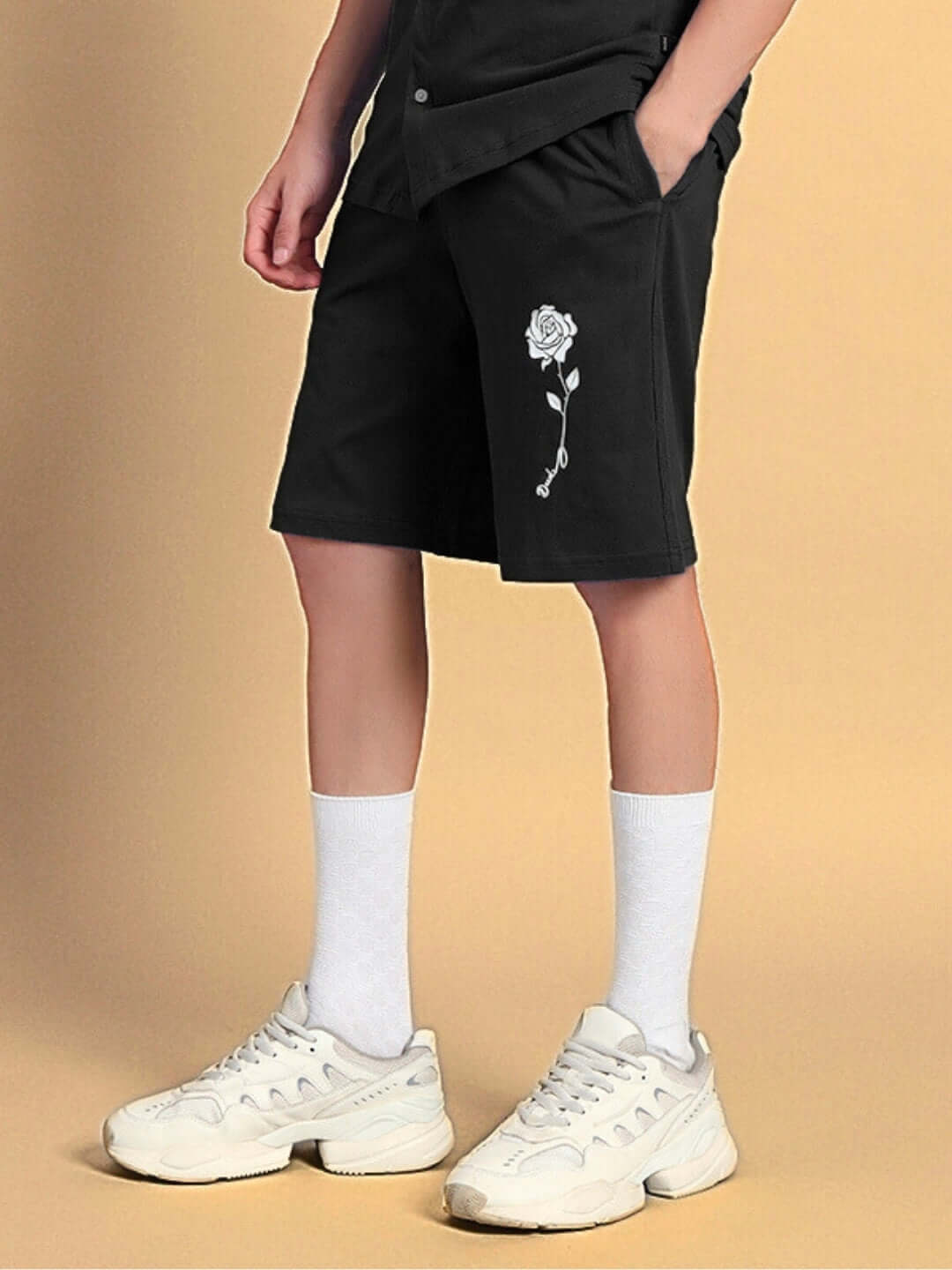 Person wearing black LIMBO Summer Shorts with rose design, showcasing casual style and custom fit option by DUDS.