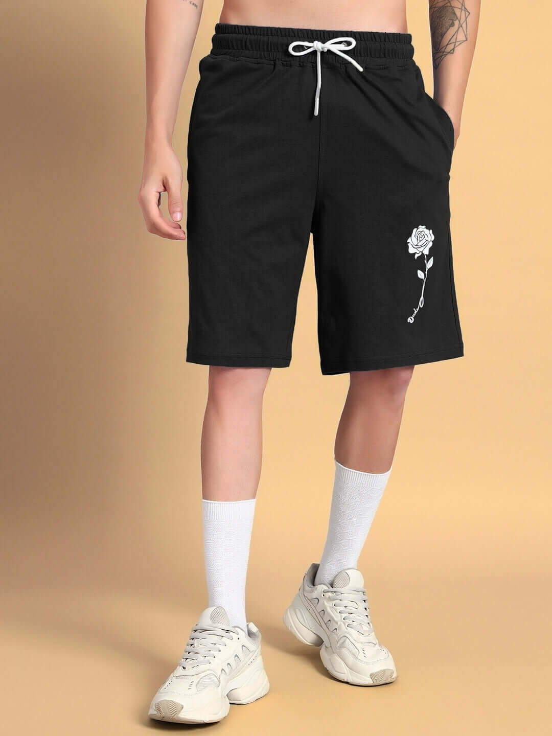 Man wearing black LIMBO SUMMER SHORTS featuring rose embroidery, paired with white sneakers and socks, showcasing casual style.