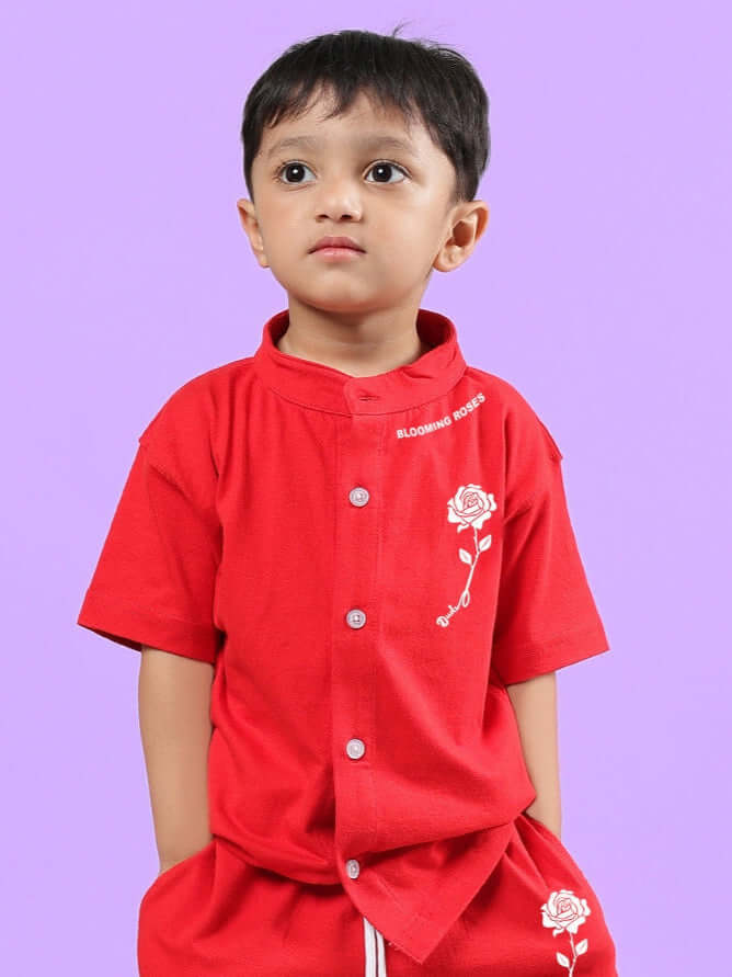 Young child wearing a vibrant red unisex Limbo Shirt from DUDS, adorned with delicate rose embroidery, standing against a purple background.