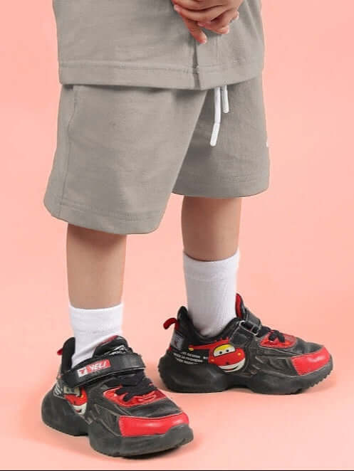 Child wearing LIMBO SHORTS FOR BOYS & GIRLS GREY paired with colorful sneakers on a pink background.