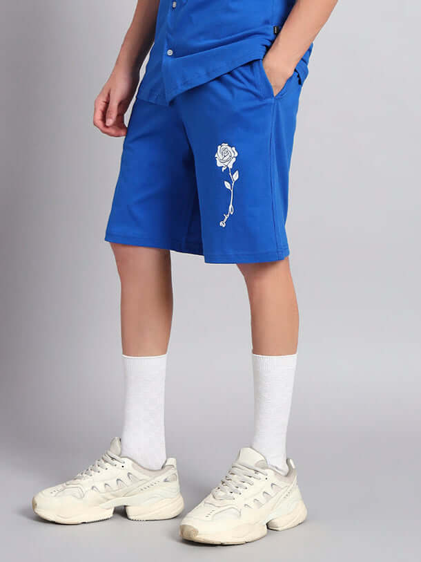 Person wearing blue LIMBO summer shorts with a white floral design, showcasing a casual style paired with white sneakers and socks.