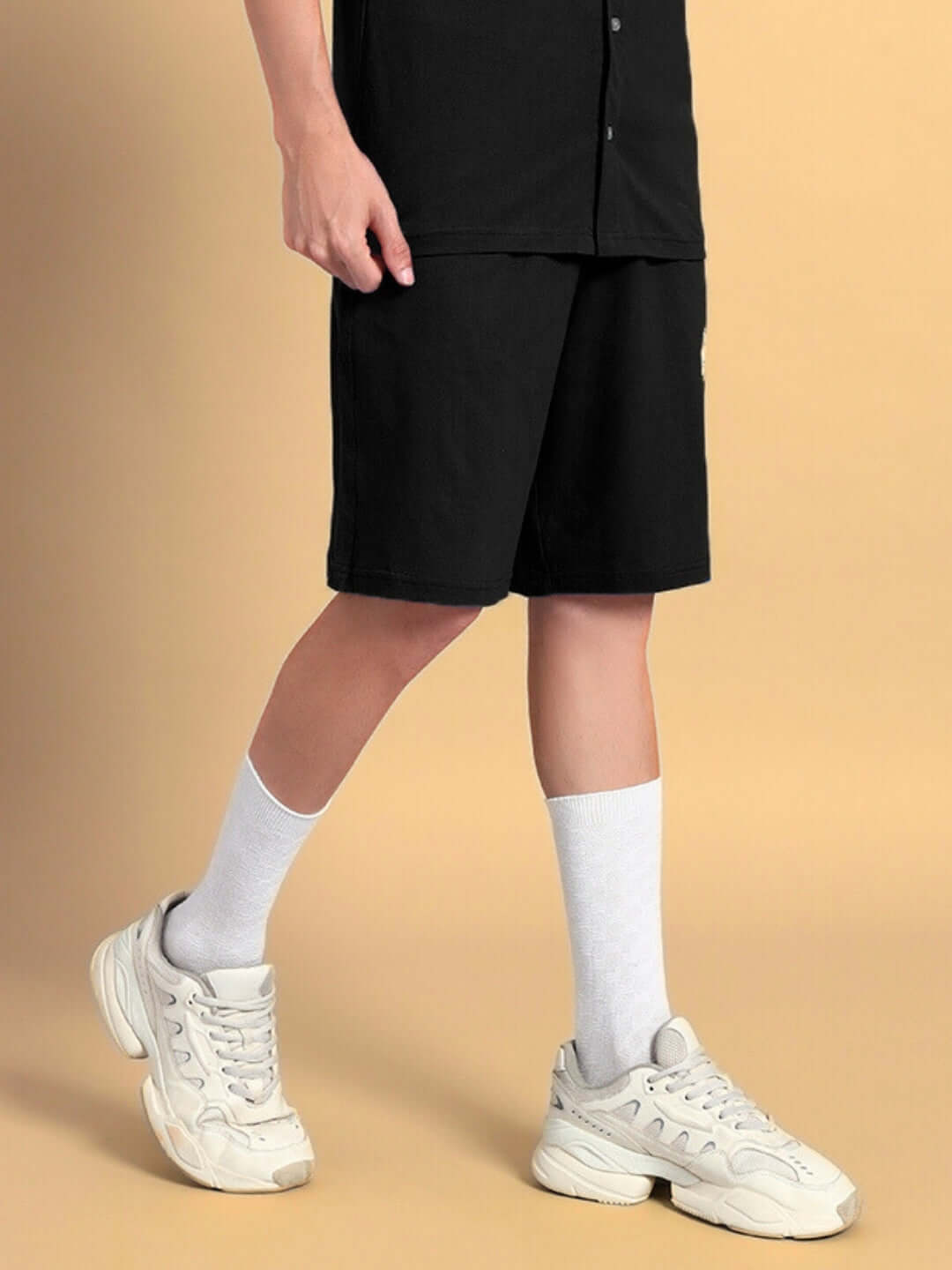 Person wearing LIMBO Summer Shorts in black with white sneakers and socks on a beige background.