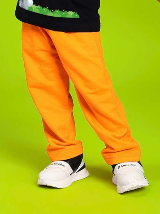 Child wearing LIMITED EDITION JOGGER FOR BOYS AND GIRLS ORANGE on bright green background, showcasing the vibrant pants.