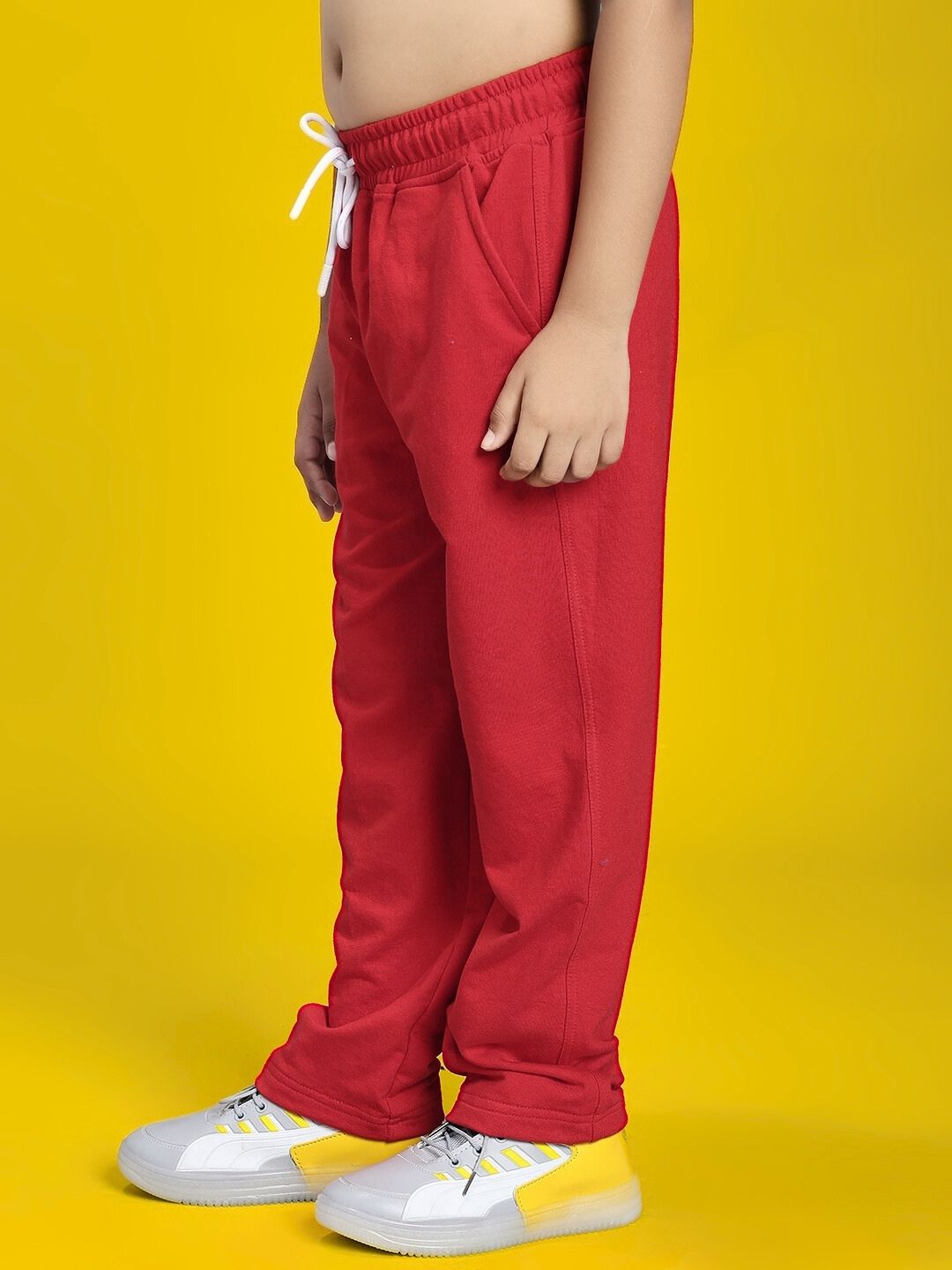 Child wearing LIMITED EDITION JOGGER FOR BOYS AND GIRLS RED with elastic waistband and white sneakers, standing on a yellow background.