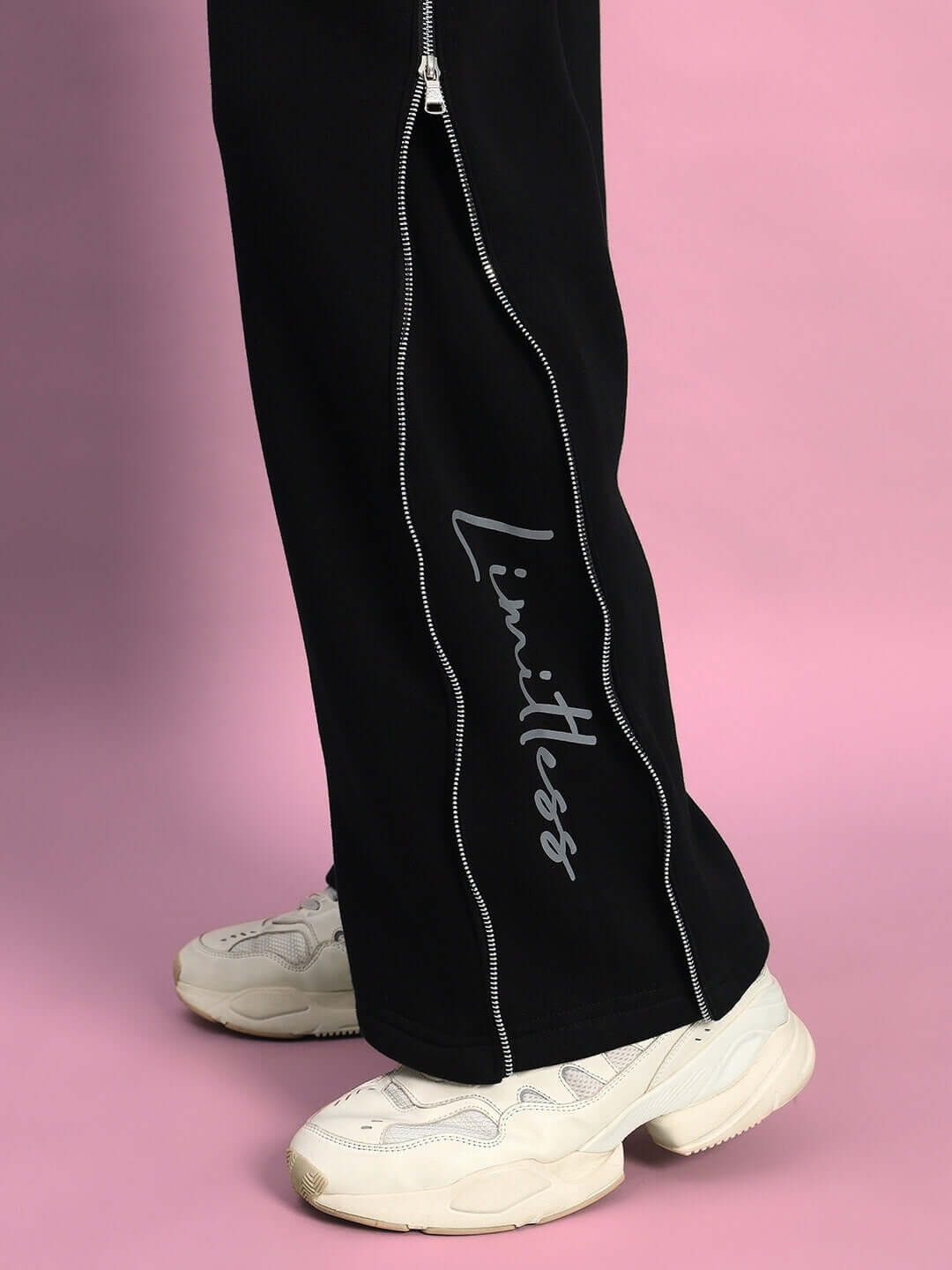 Close-up of LIMITLESS FLEECE REFLECTOR JOGGER BLACK with reflective detailing and white sneakers on pink background
