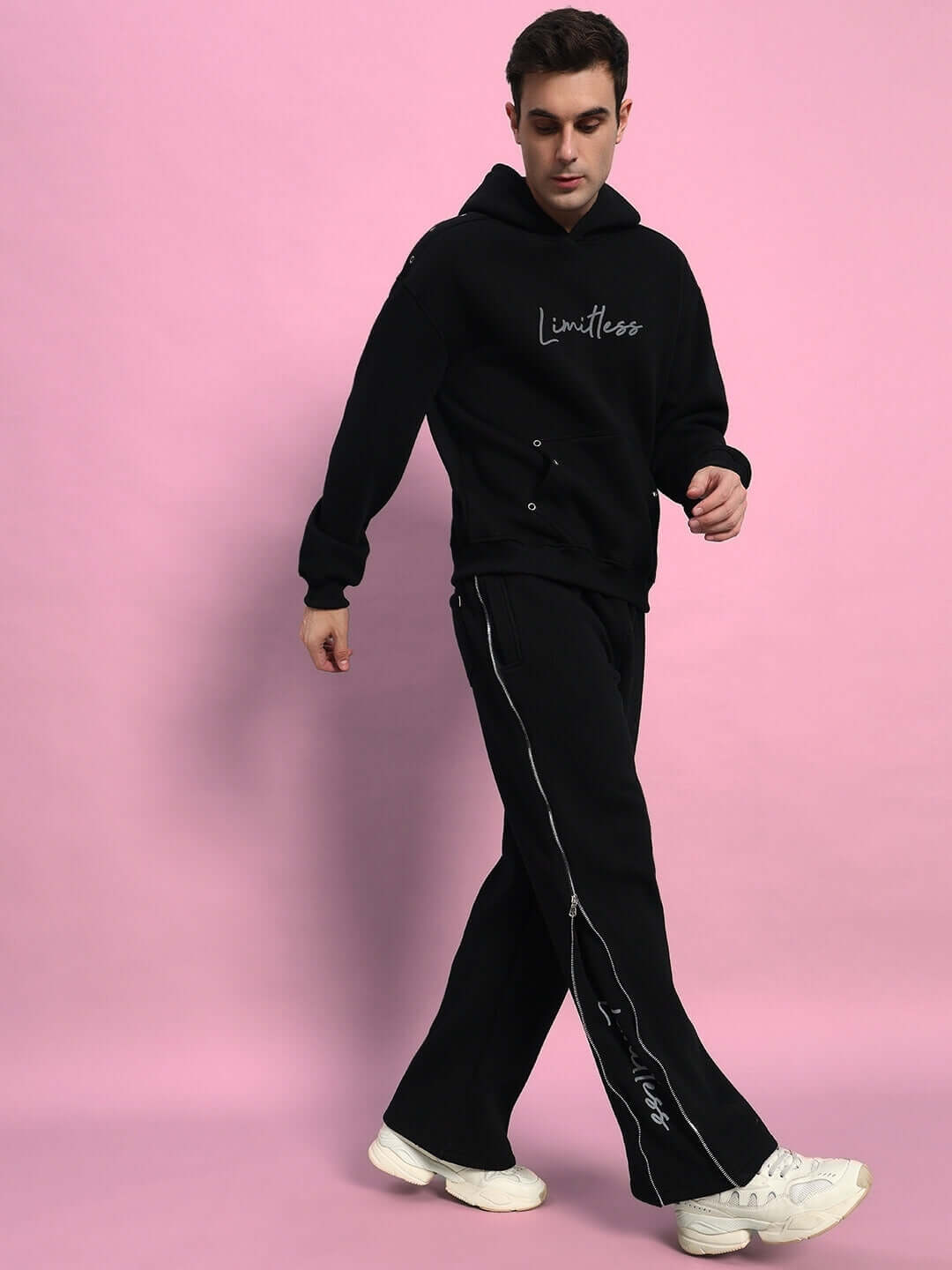 Man wearing black Limitless Fleece Reflector Jogger pants with a matching hoodie on a pink background.