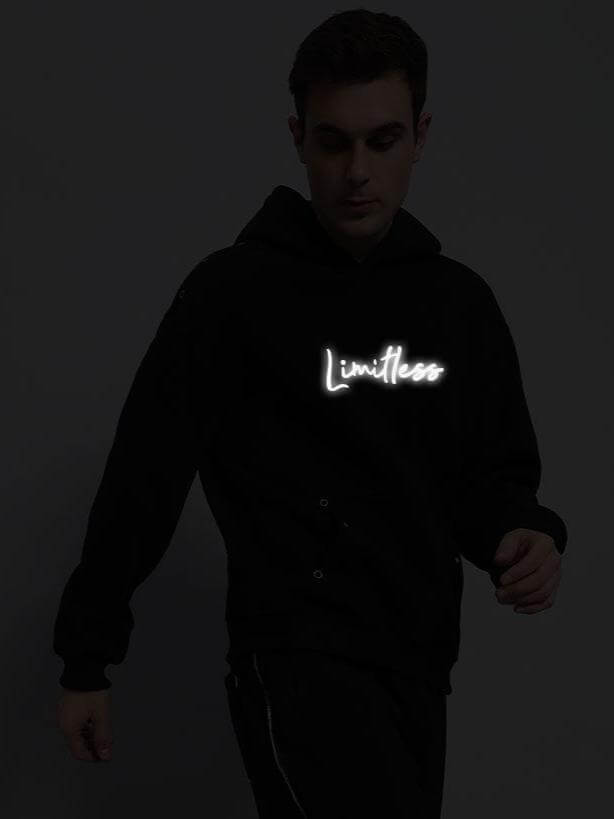 Model wearing LIMITLESS FLEECE REFLECTOR HOODIE in black, featuring luminous logo design, perfect for night visibility and style.