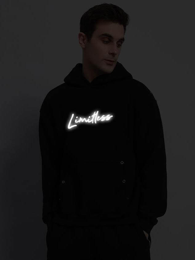 Person wearing Limitless Fleece Reflector Hoodie in Black with glowing neon text on front, stylish casual wear for cool weather.