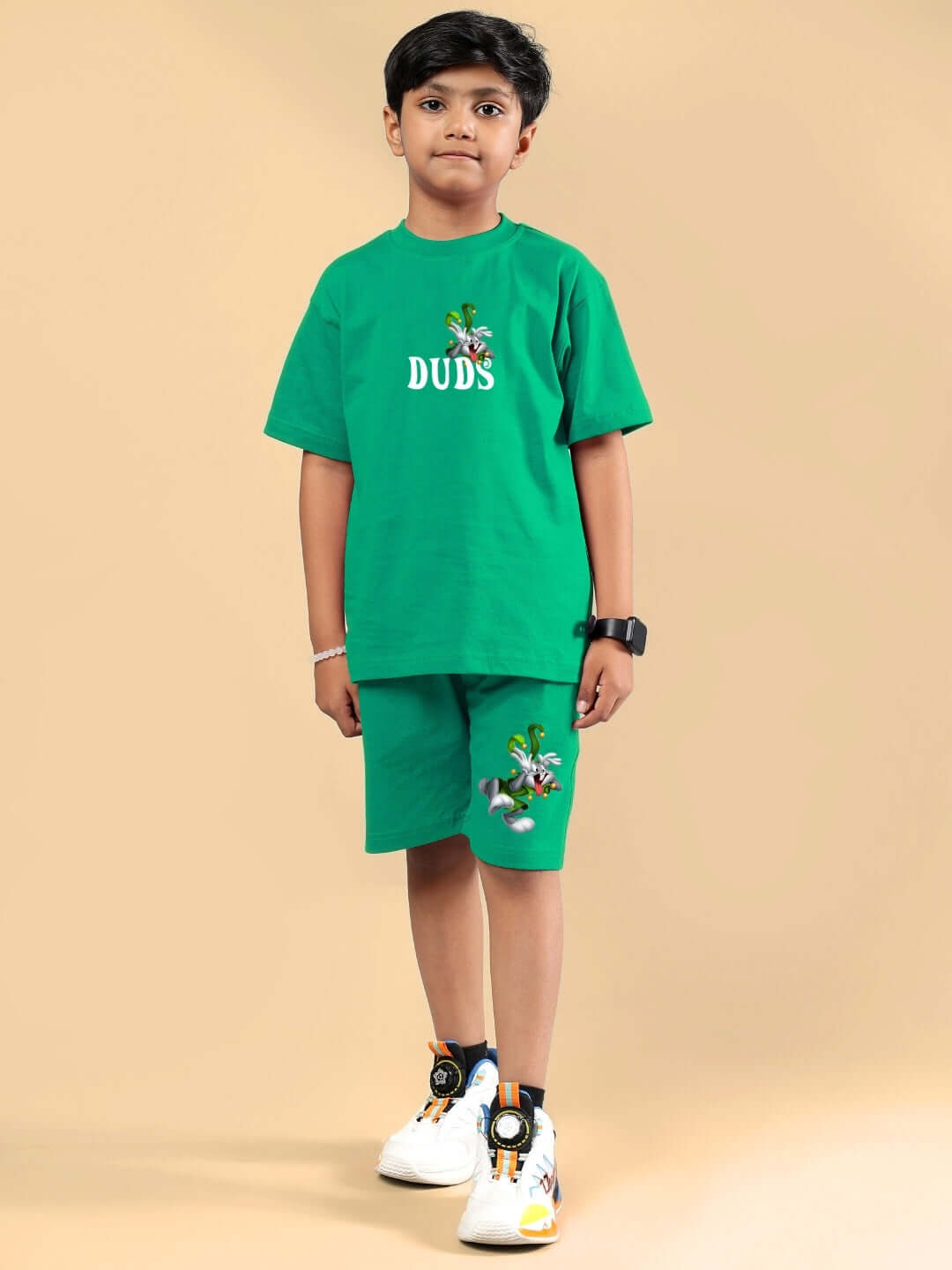 Child wearing LOONEY TUNES PRINTED SHORTS FOR BOYS & GIRLS GREEN standing against beige background